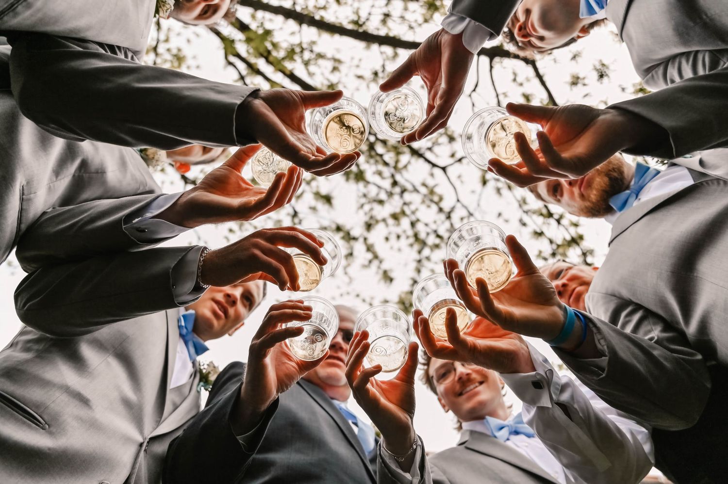 Groomsmen in grey suits form a circle looking down at the camera.