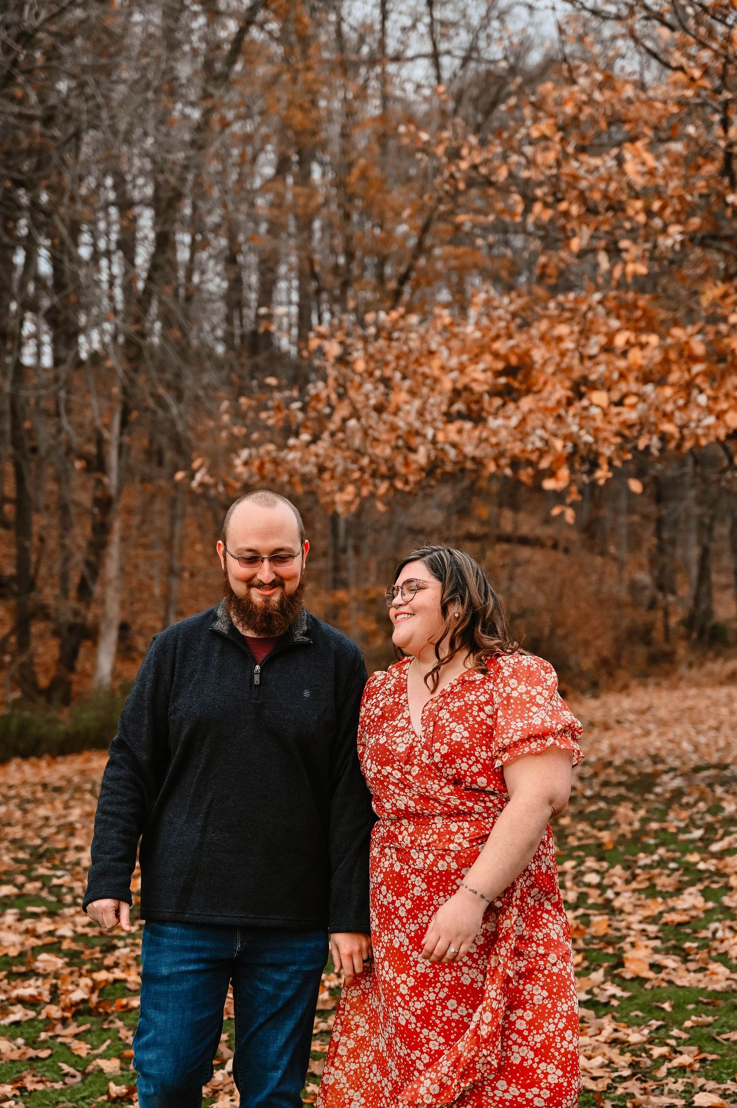 Couple laughing together during fall engagement session with orange autumn leaves.