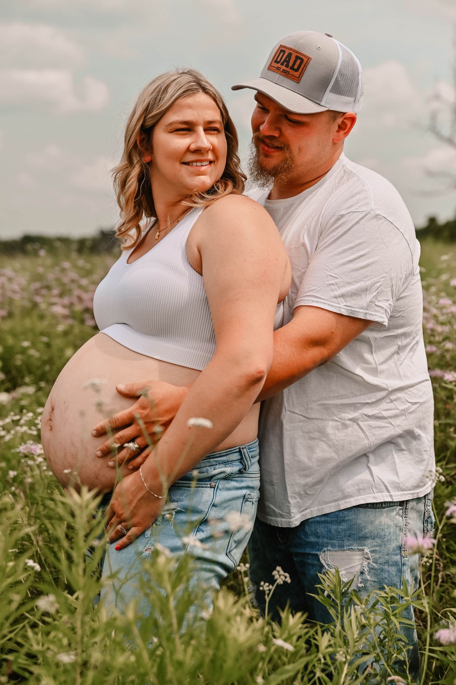 A maternity photoshoot in a wildflower field with casual summer outfits.