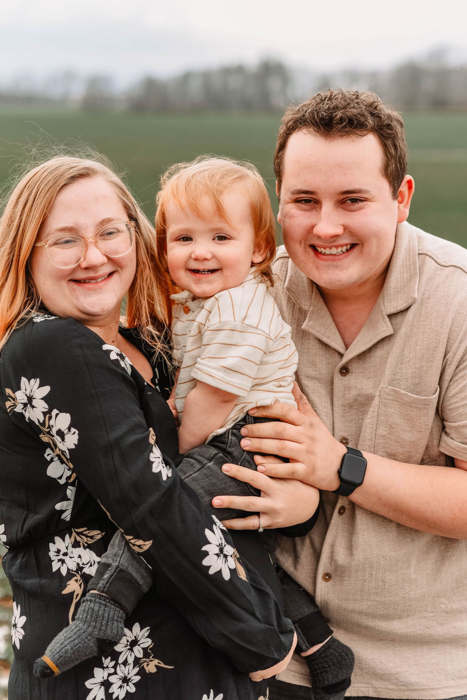 Family laughing and embracing during outdoor photo session in a field.