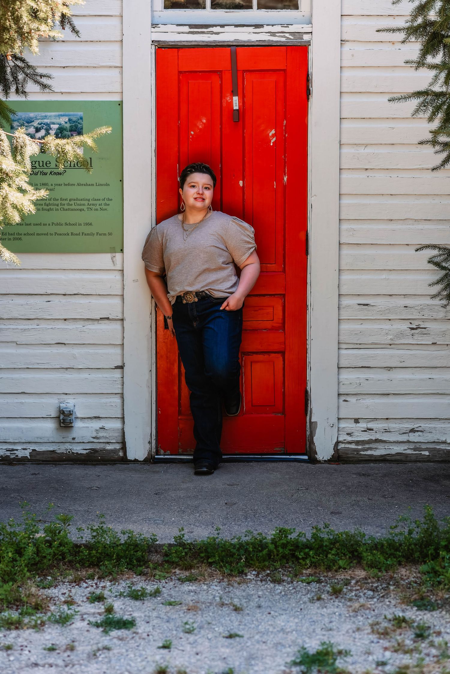 A casual portrait in front of a bright red door on a white building.