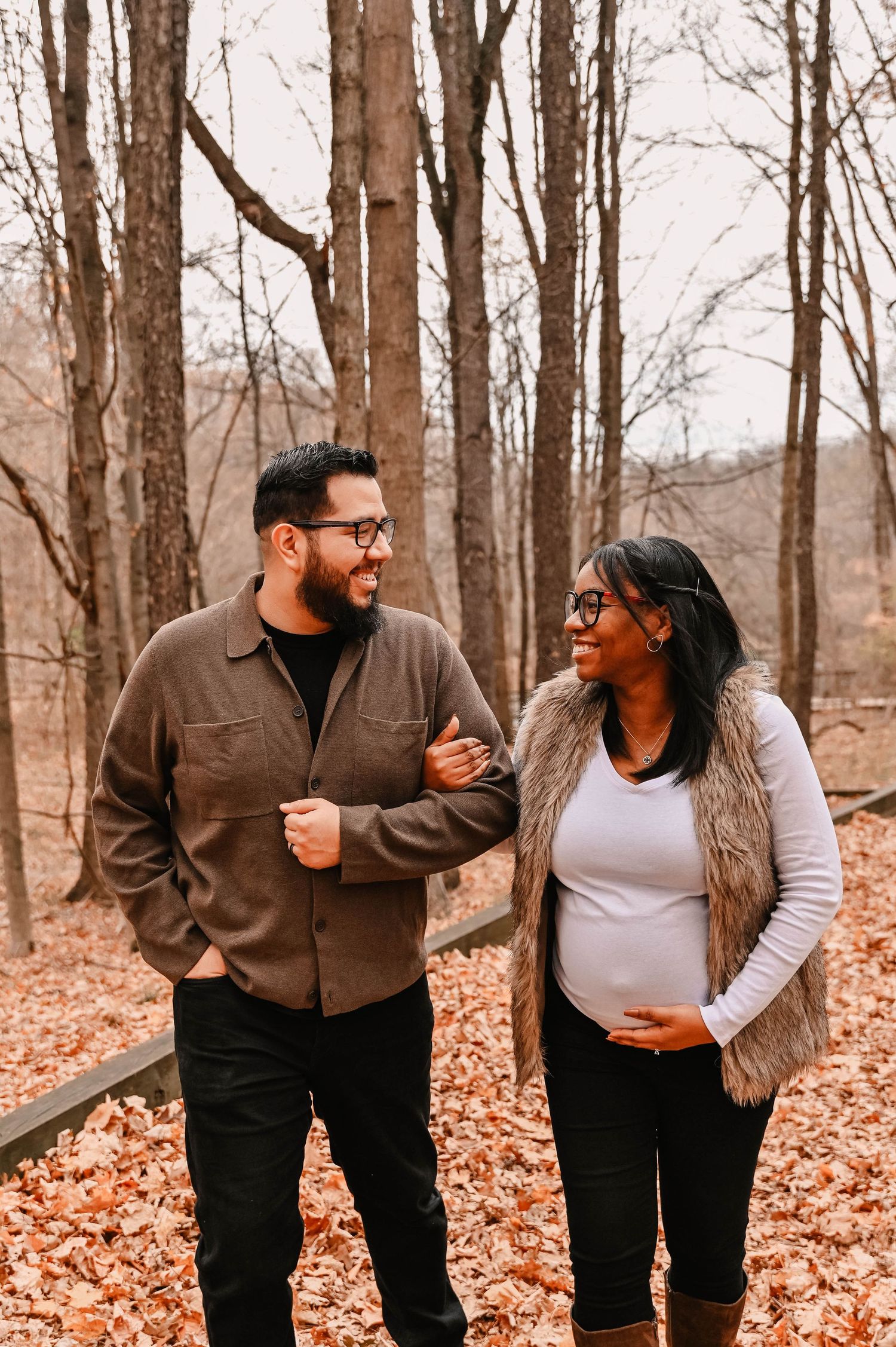 Couple walking together on leaf-covered path in autumn woods.
