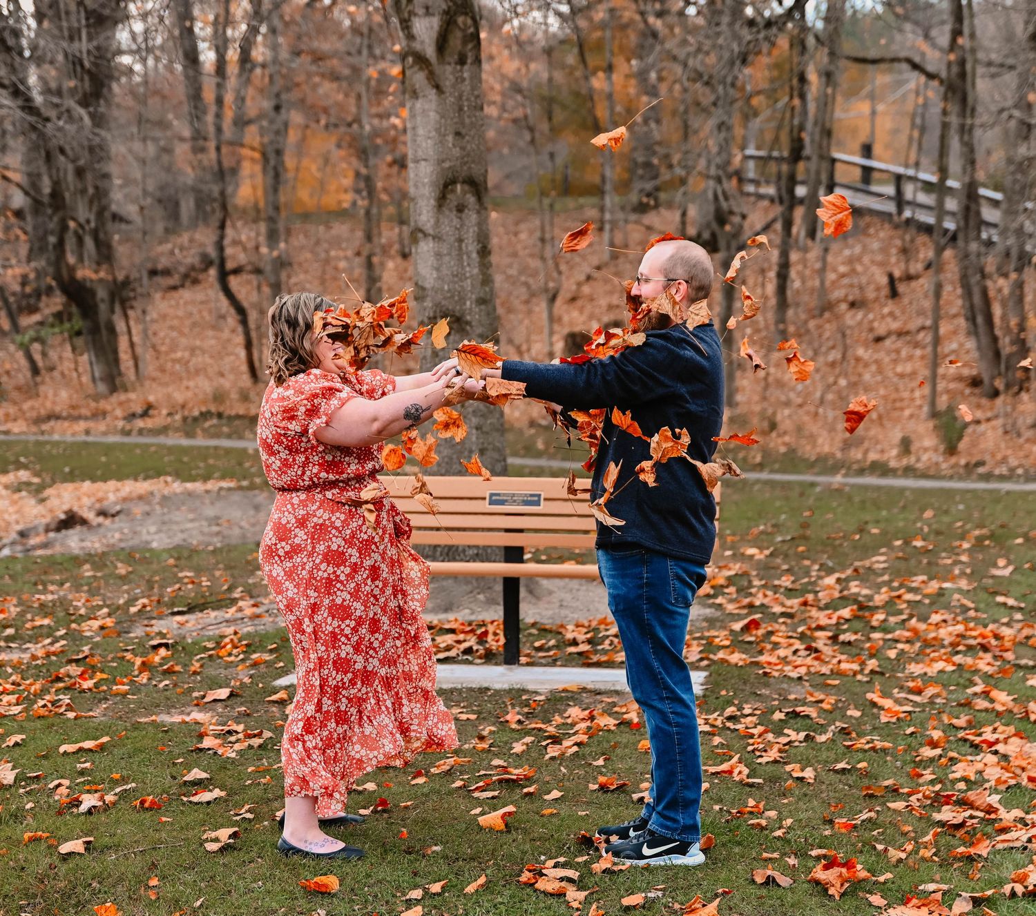 Playful couple throwing autumn leaves during fall engagement photoshoot.