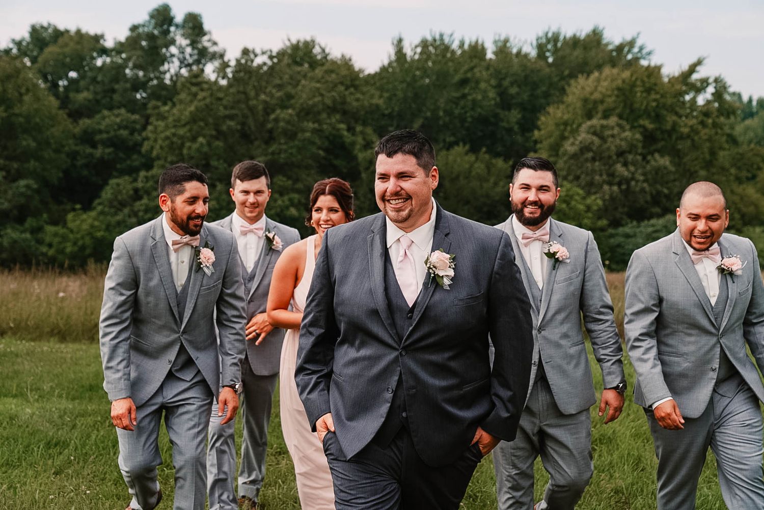 Groomsmen walking and laughing together outdoors in matching gray suits.
