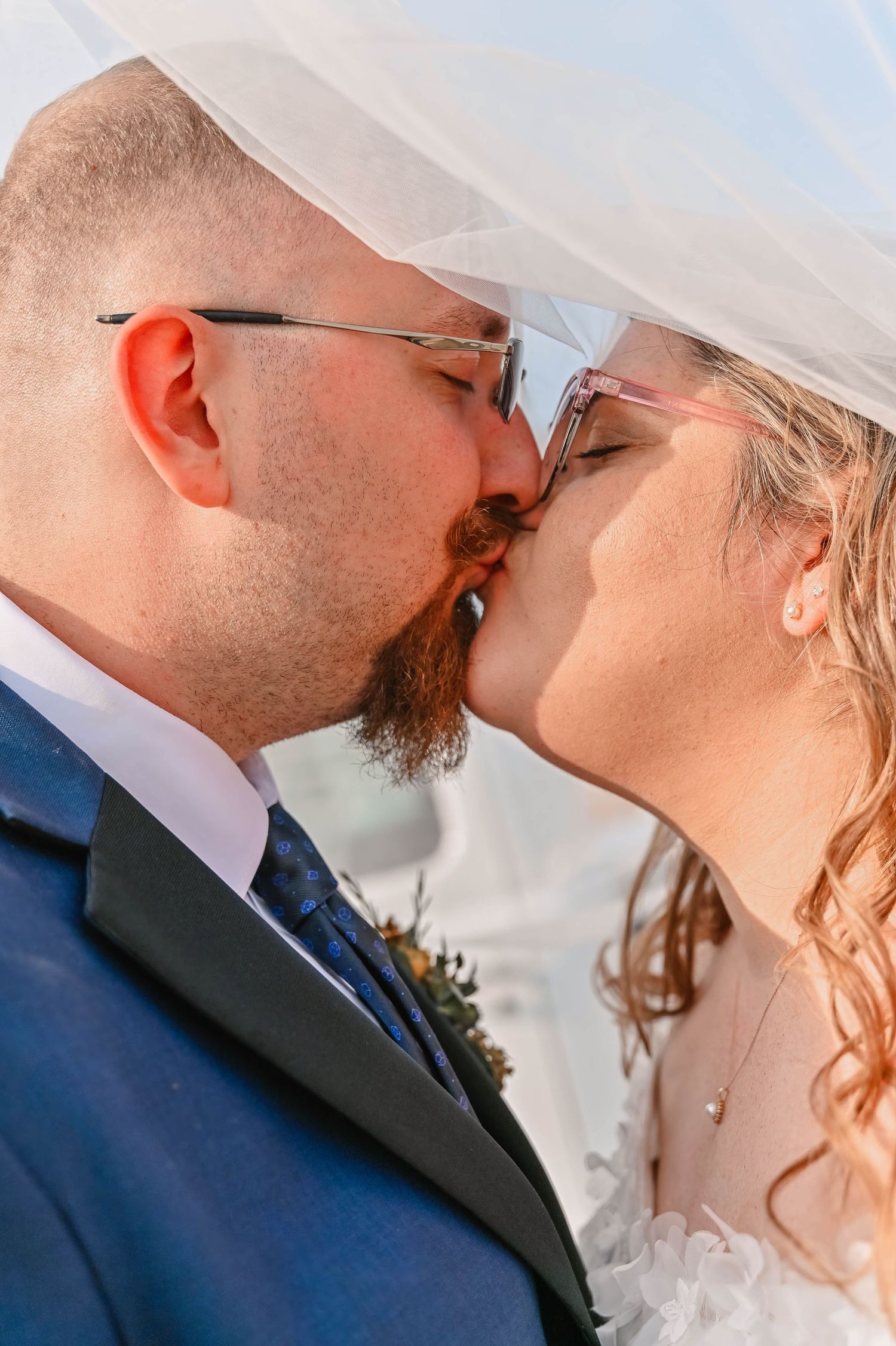 Romantic wedding moment captured under a white veil against blue sky.