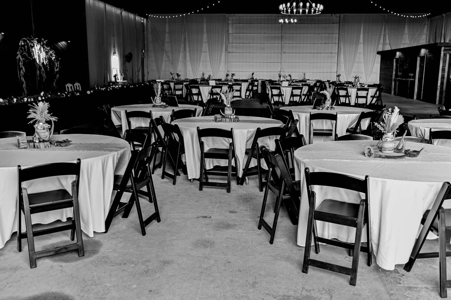 Black and white photo of an empty wedding reception setup with round tables and folding chairs.