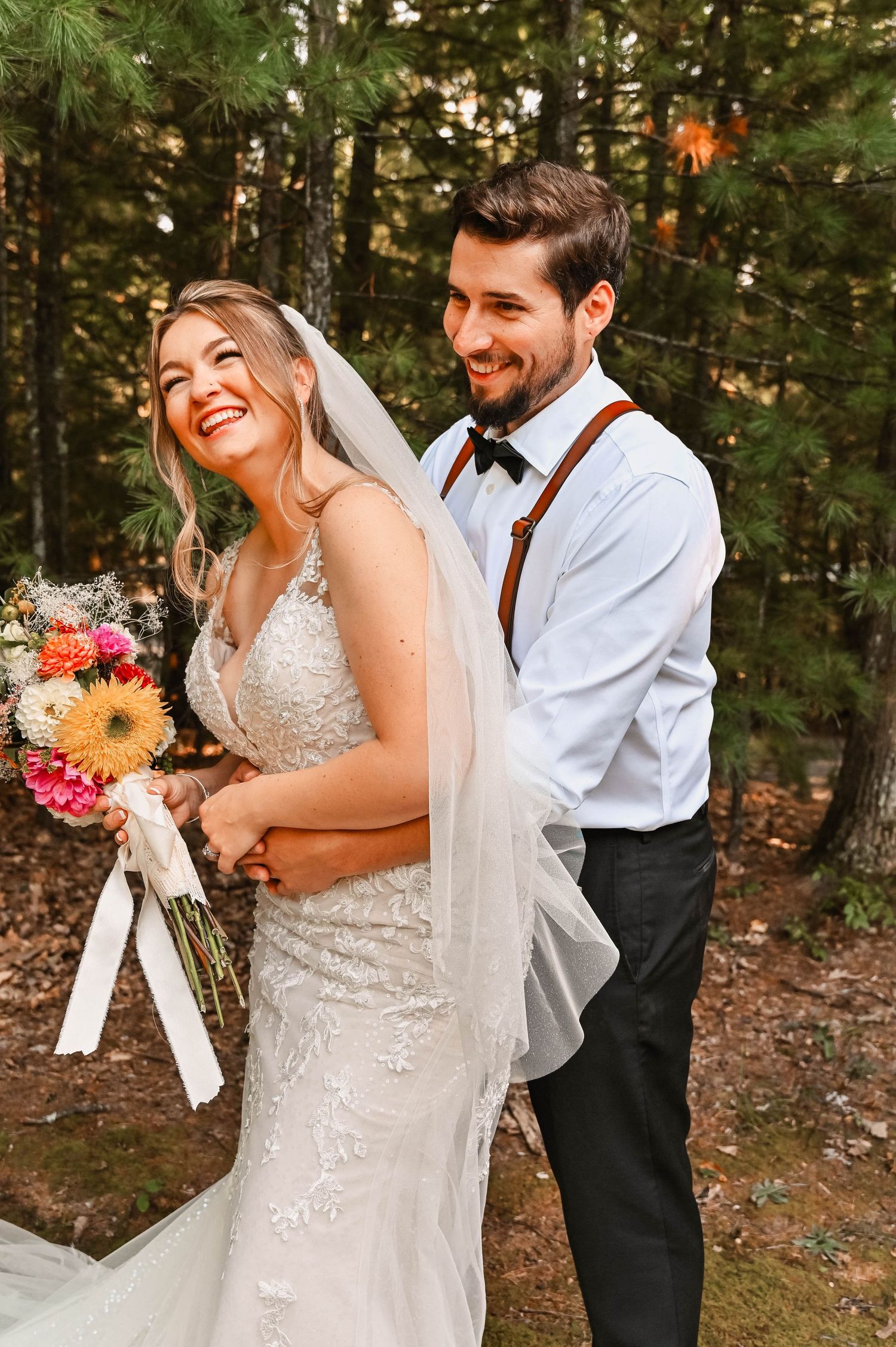 Newlyweds share joyful moment in forest setting with colorful bouquet.