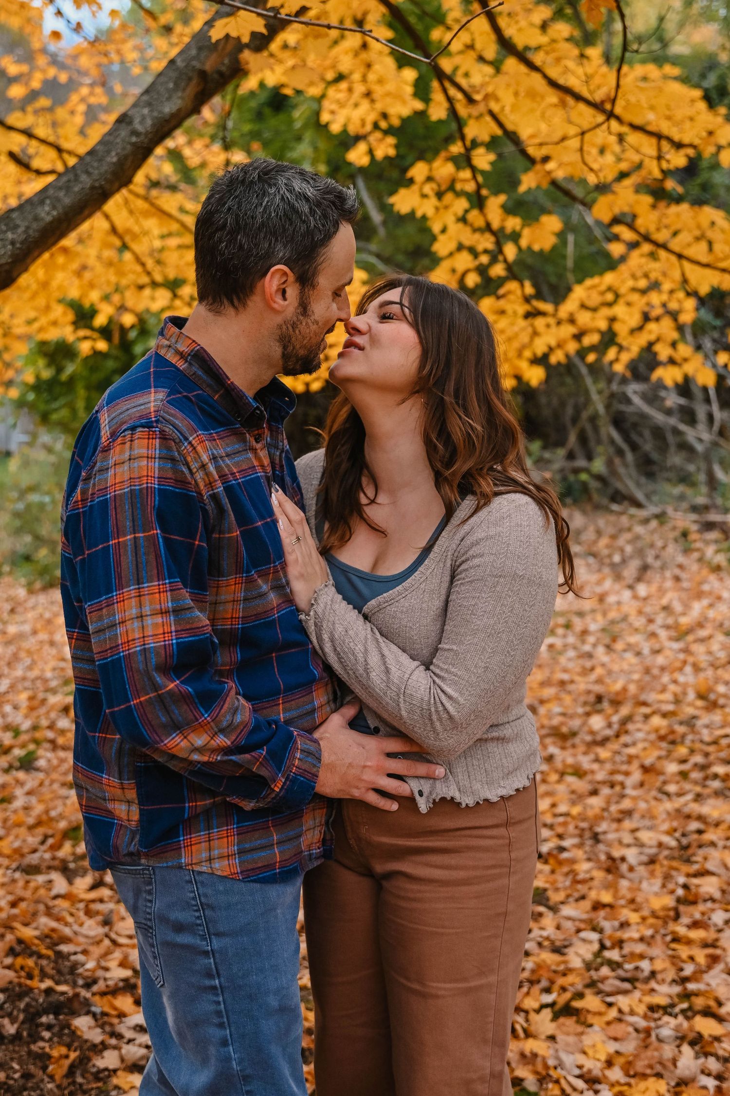 Romantic autumn moment captured under golden maple trees with fallen leaves.