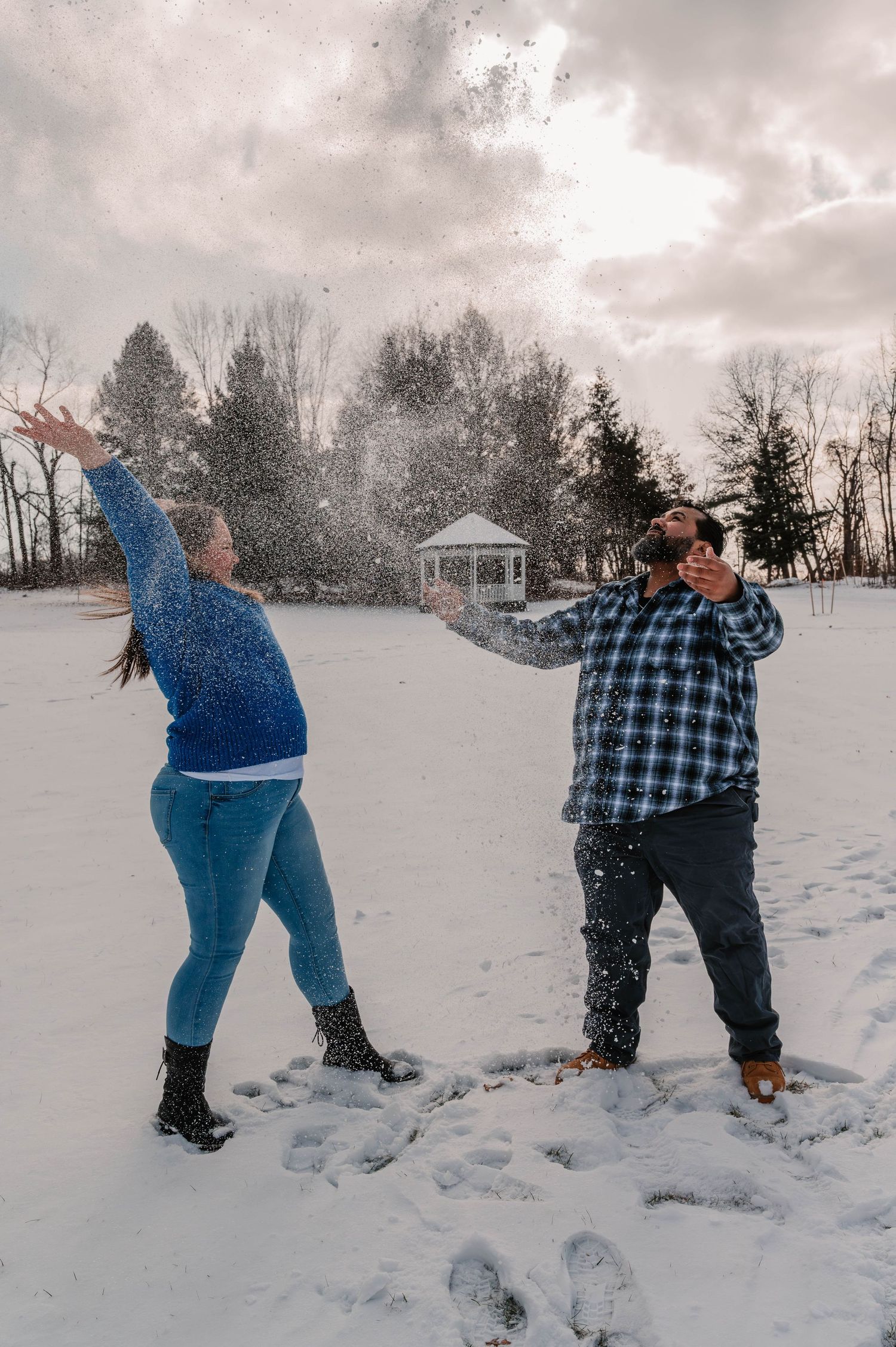 Playful snow fight between two people in winter landscape with trees and gazebo.