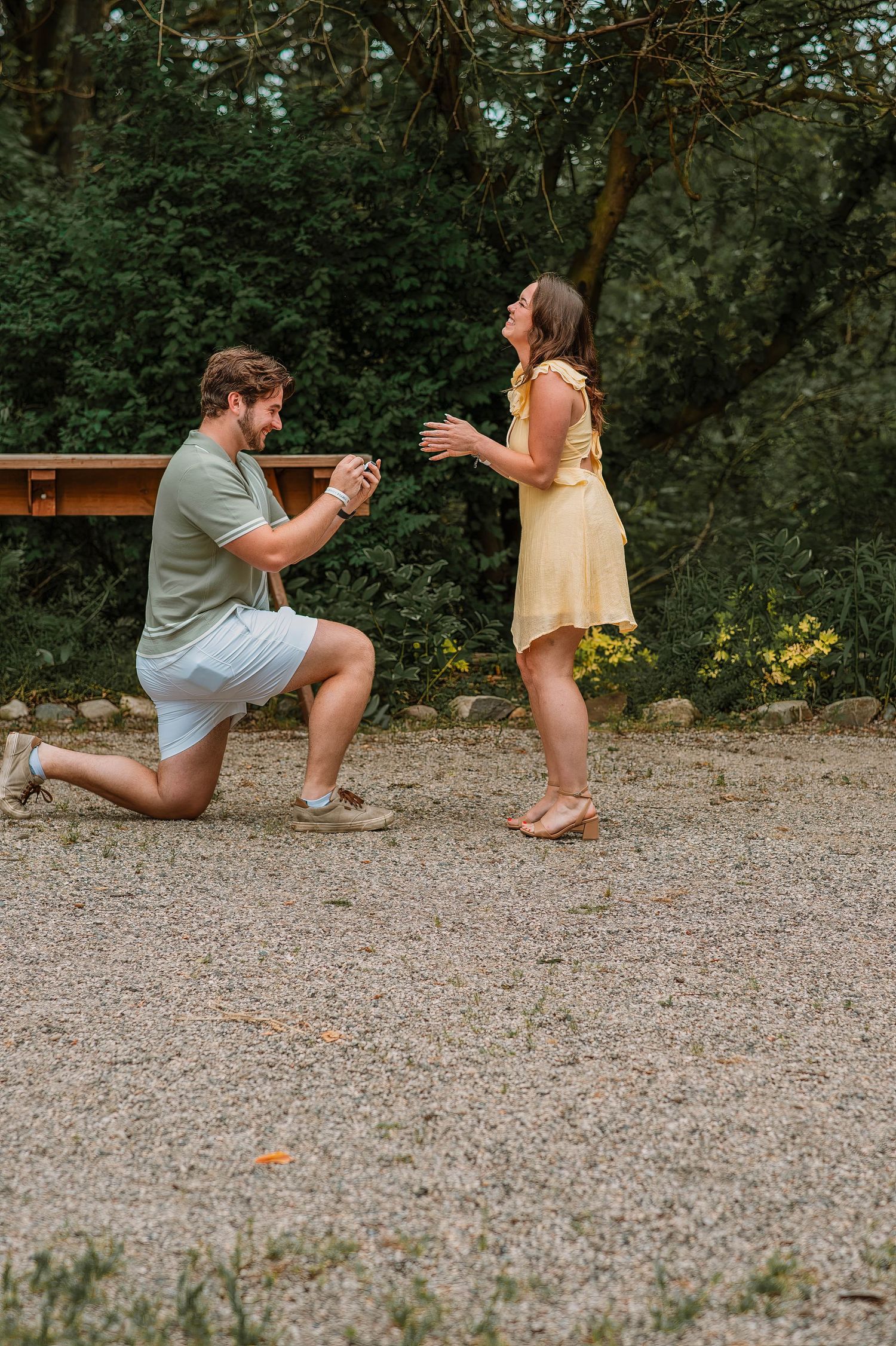 A surprise proposal moment captured on a gravel path outdoors.