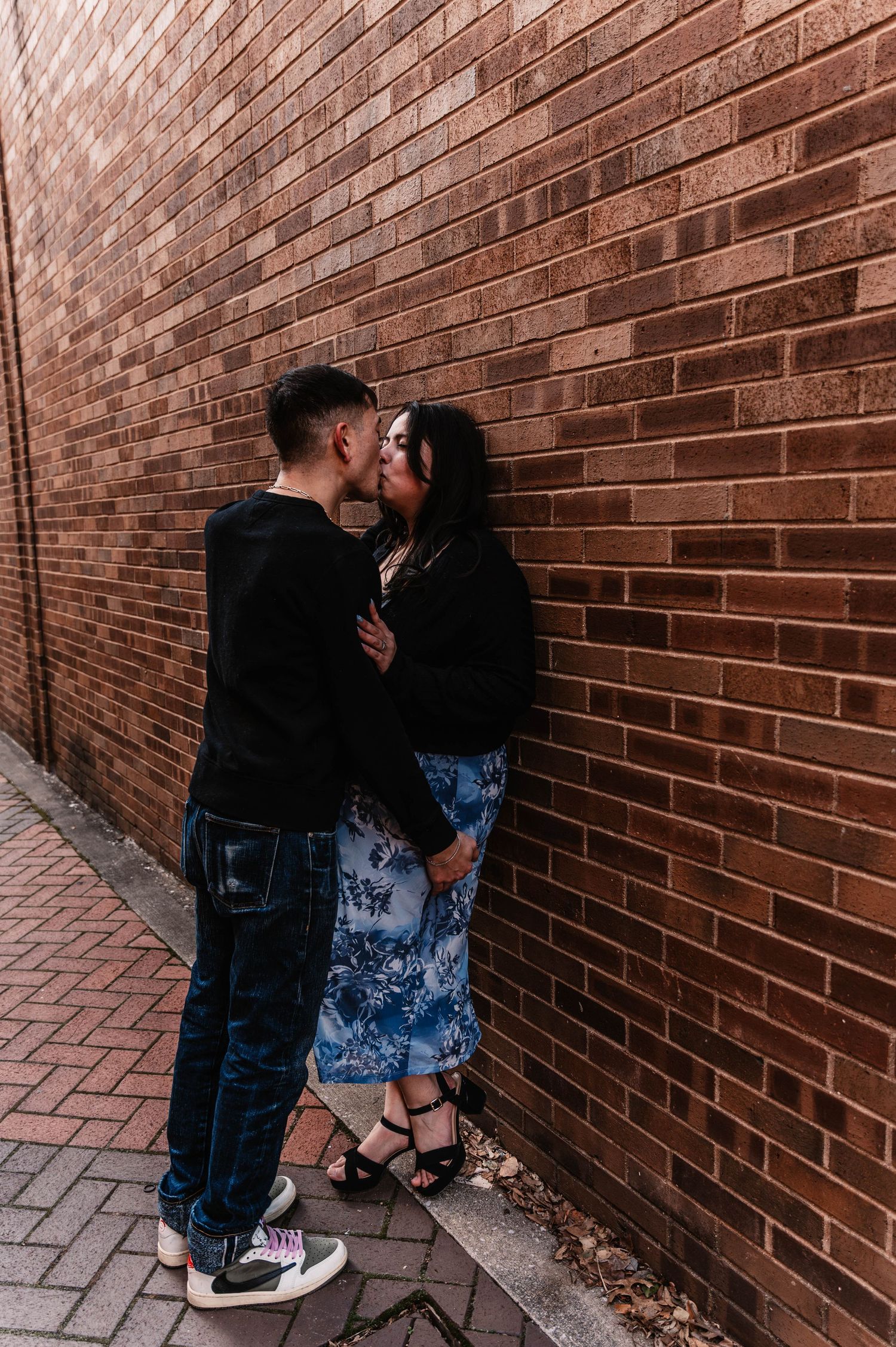 A couple shares an intimate moment against a rustic brick wall background.