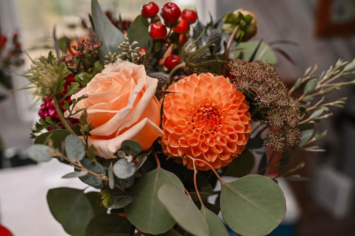 Floral arrangement with orange dahlias, roses, and red berries.