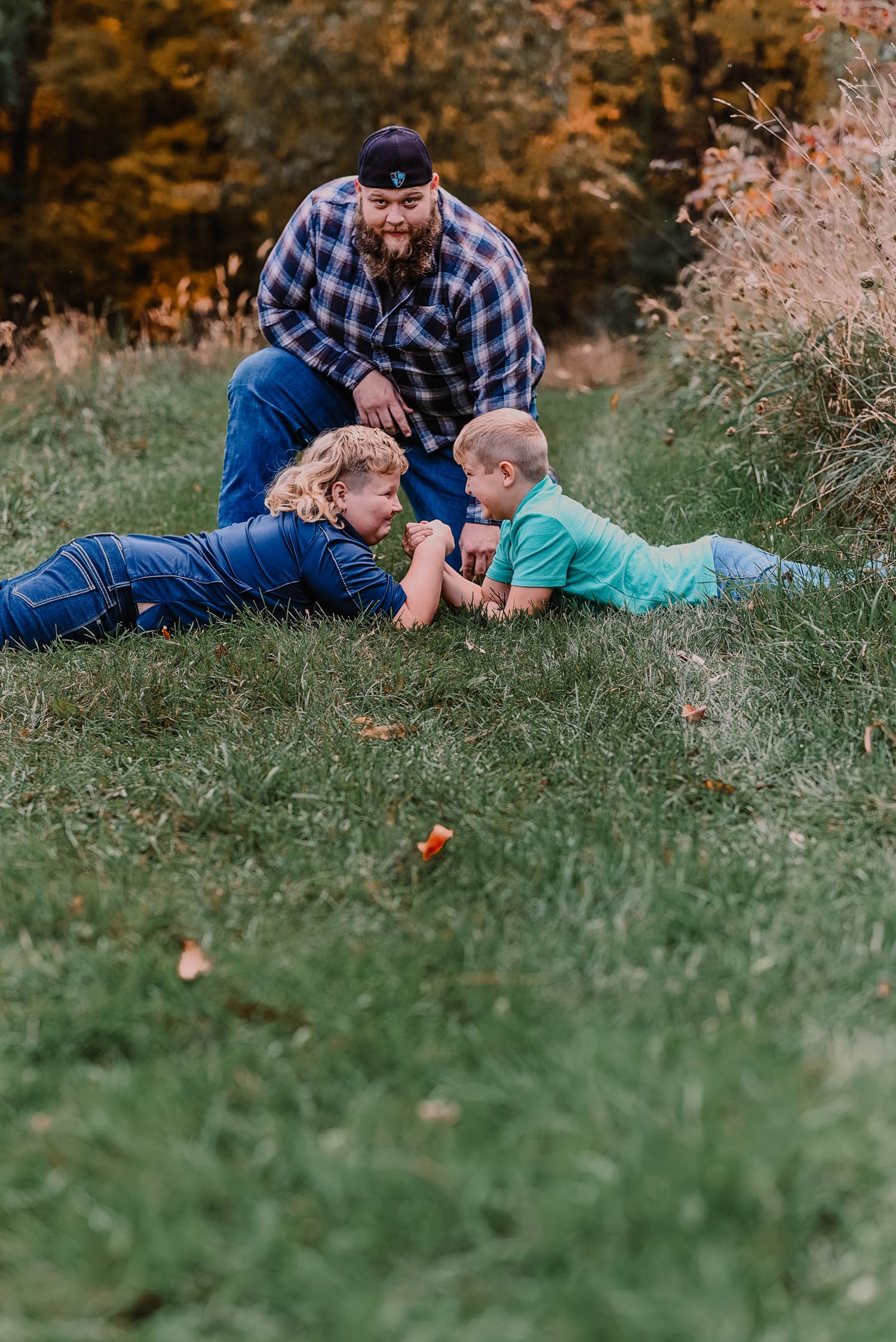 Family playfully lounging on autumn grass with fall foliage in background.