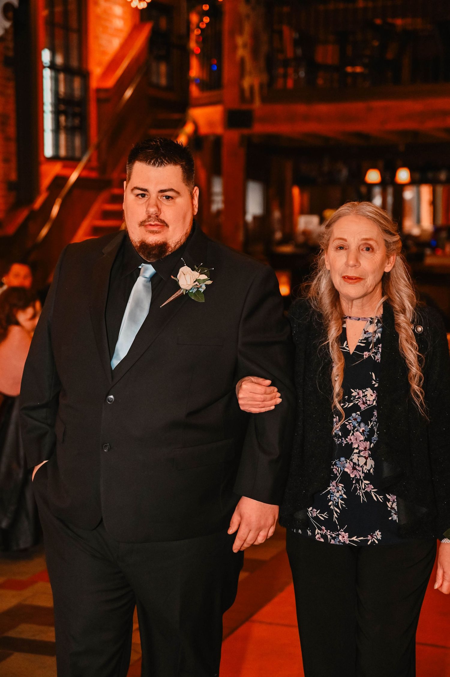 Couple poses together in formal attire under warm orange lighting at evening event.