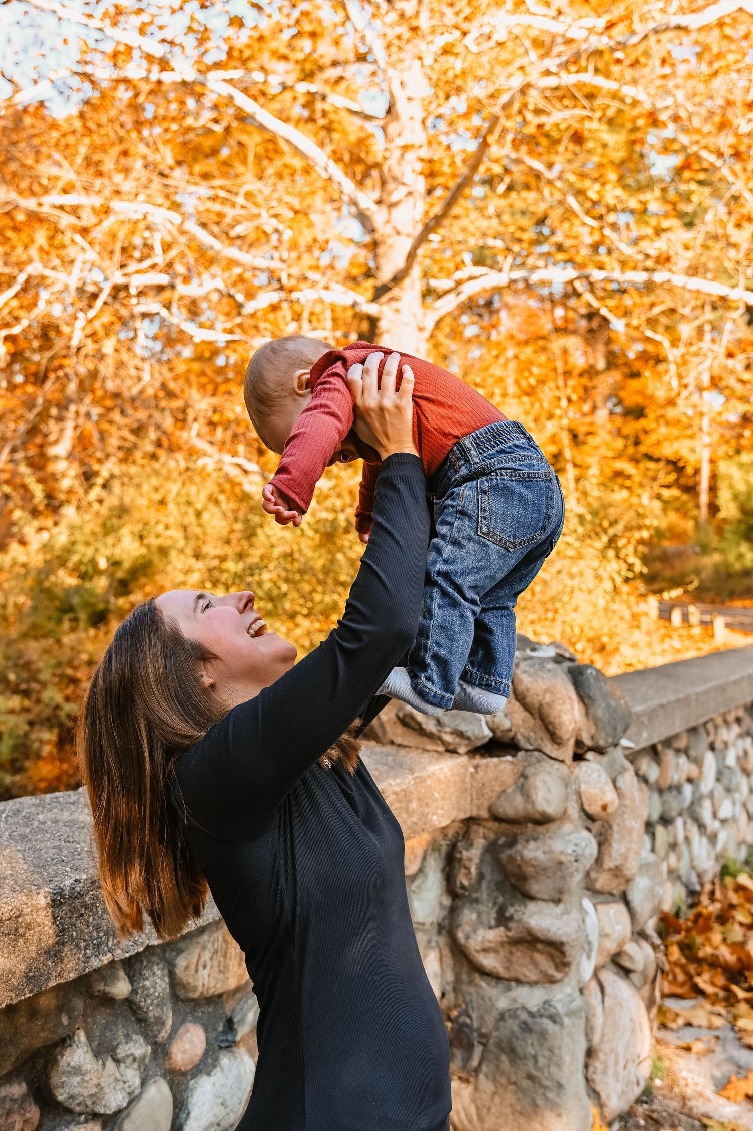 Playful moment between parent and child against backdrop of golden autumn trees.