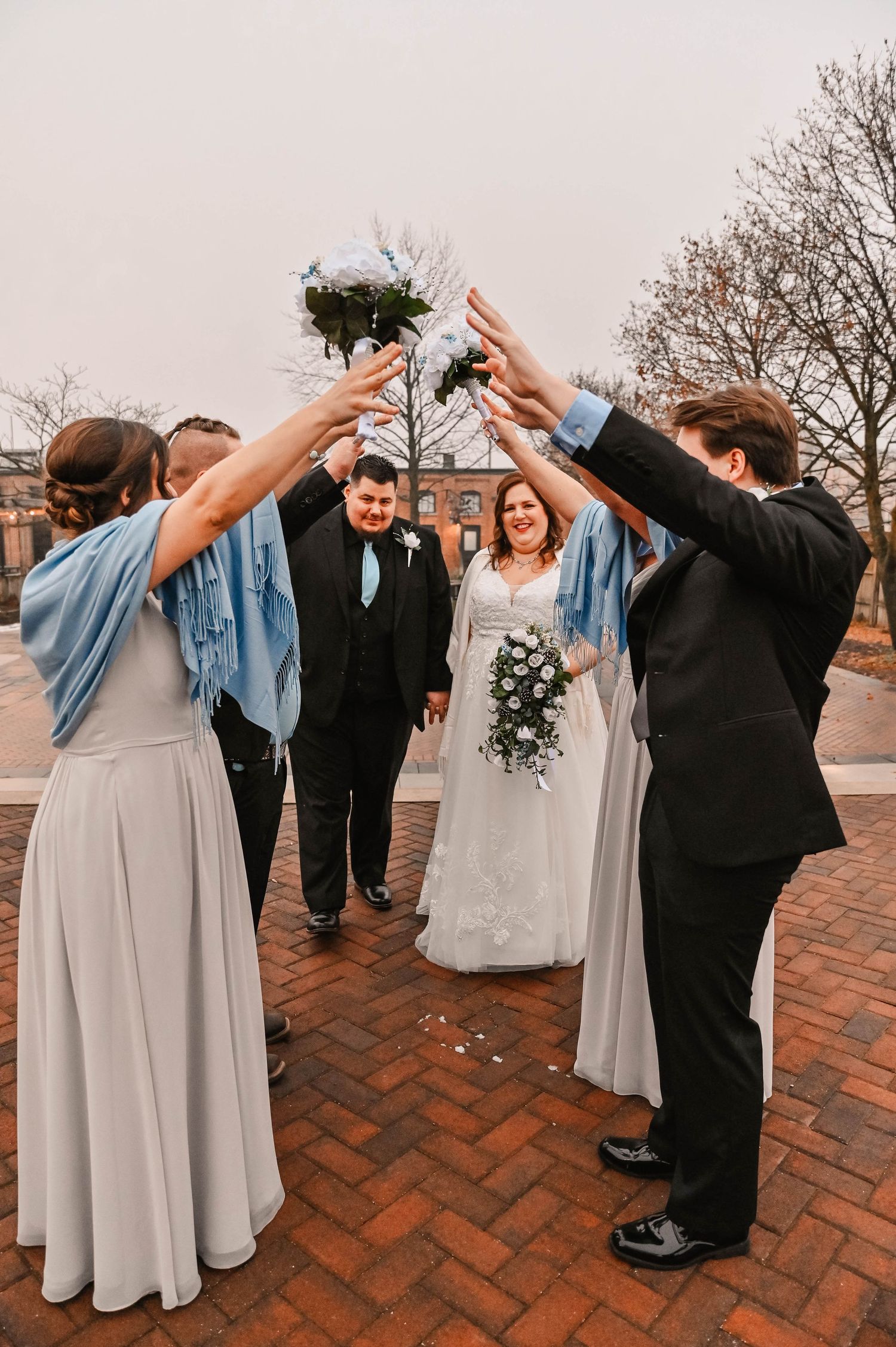 Wedding party members pose for fun photos on a brick patio outside.