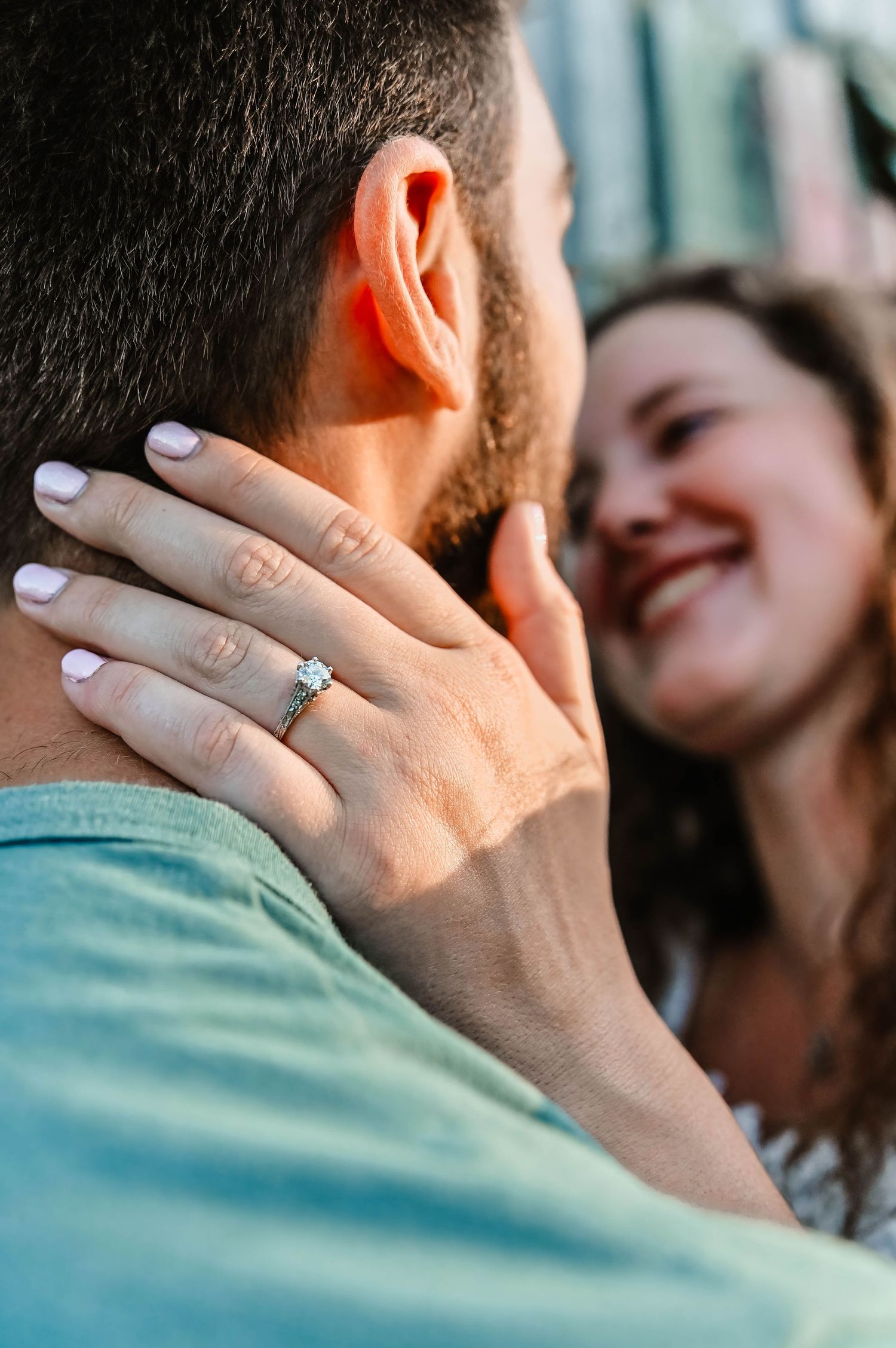 Close-up of hand with engagement ring caressing face against teal shirt.