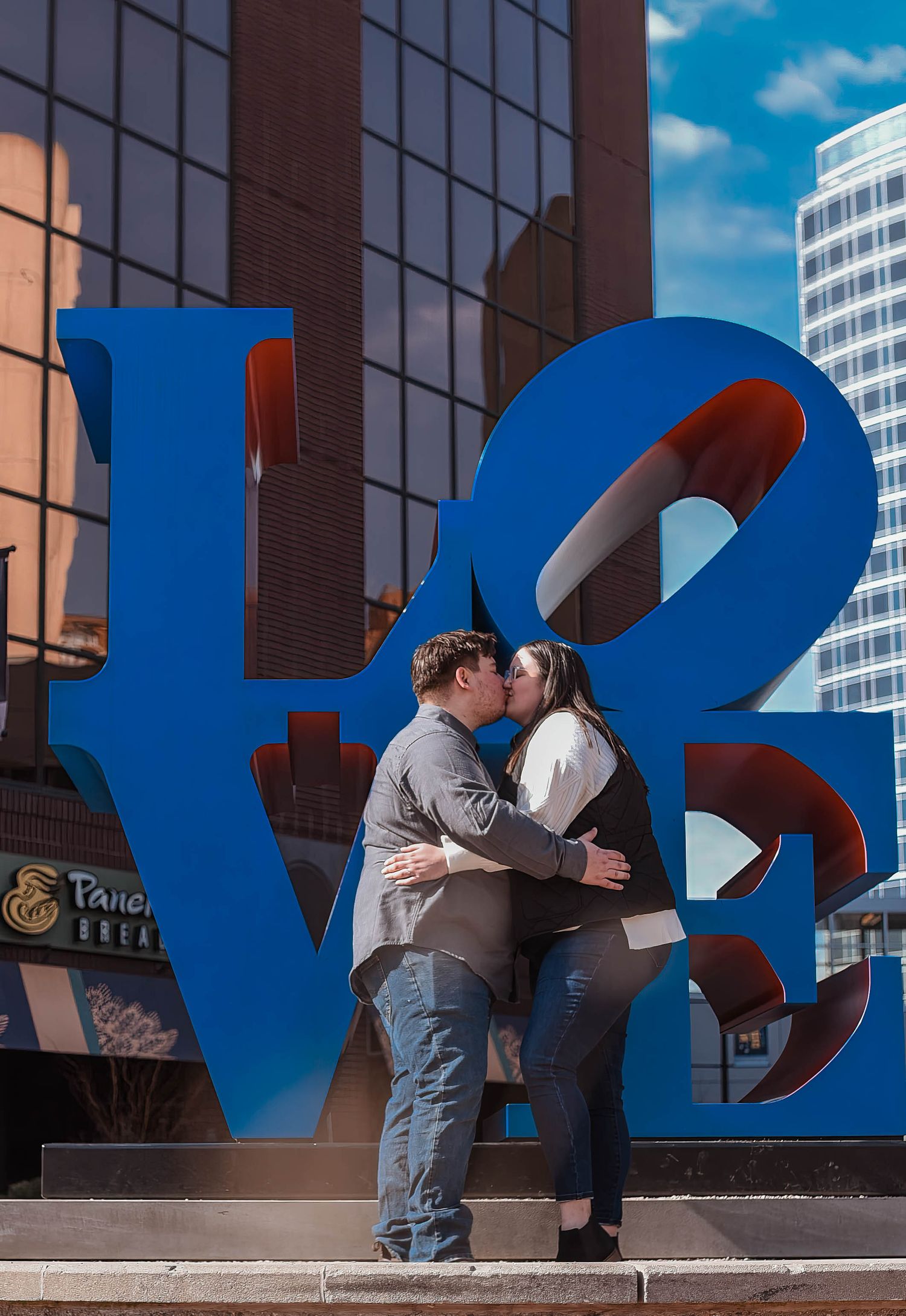 A couple embracing in front of large blue letters on an urban building wall.