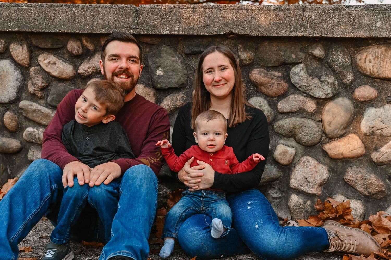 Family sitting together on stone wall during outdoor photo session.