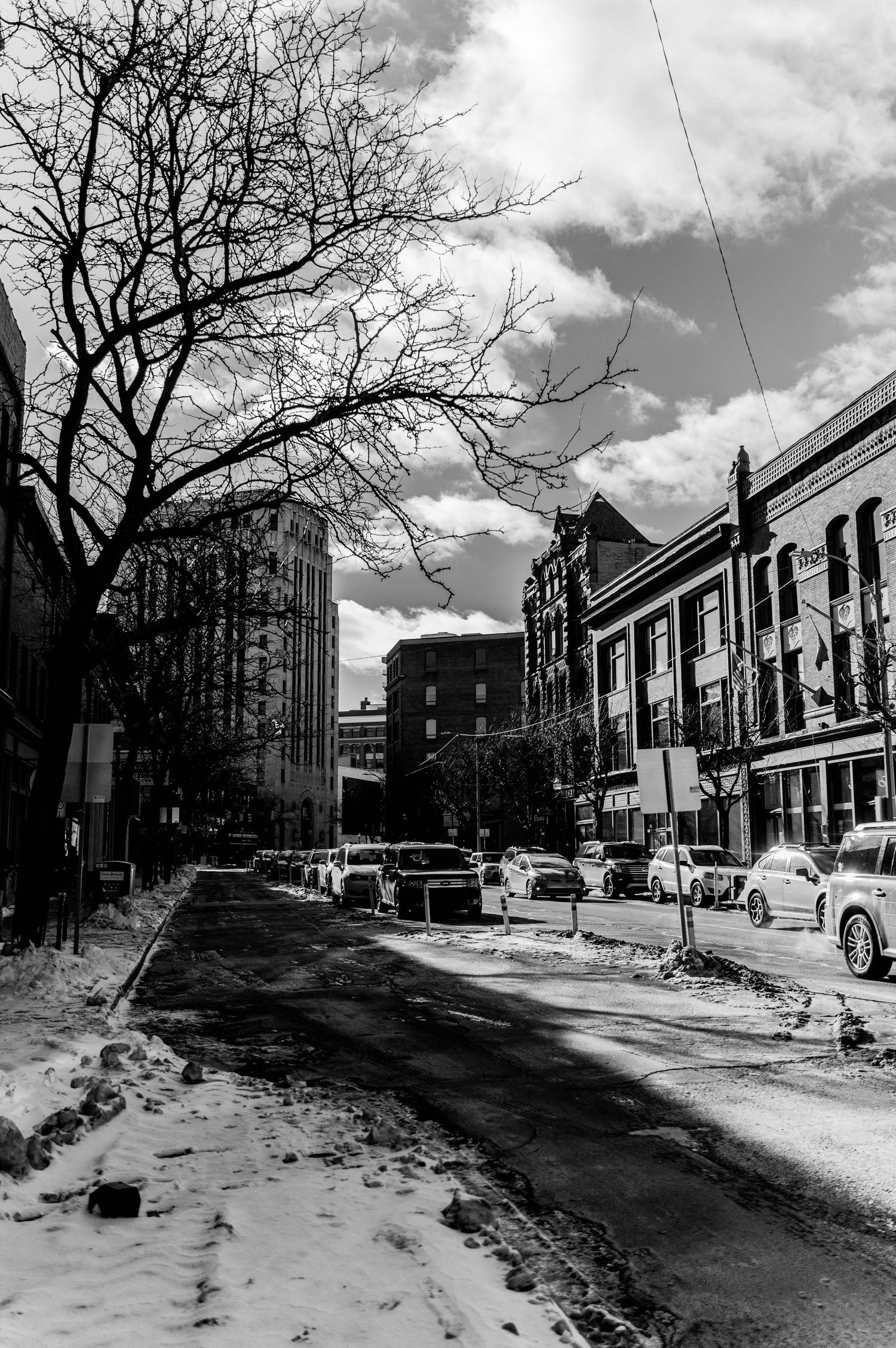 Black and white winter street scene showing snowy urban neighborhood with parked cars.