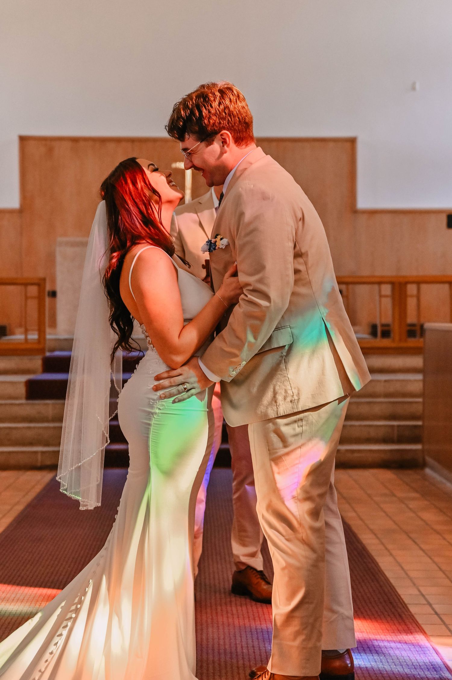 Newlyweds share romantic first dance under colorful lighting in reception hall.