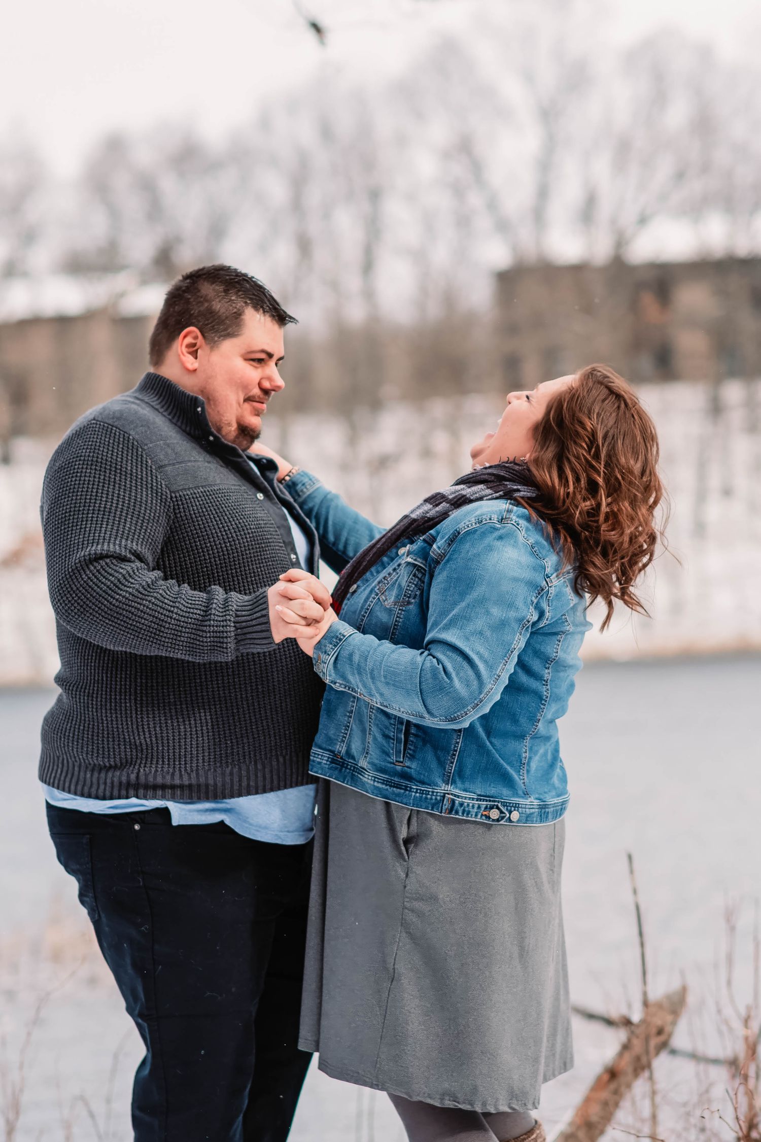 Playful couple in winter clothing posing by a frozen lake.