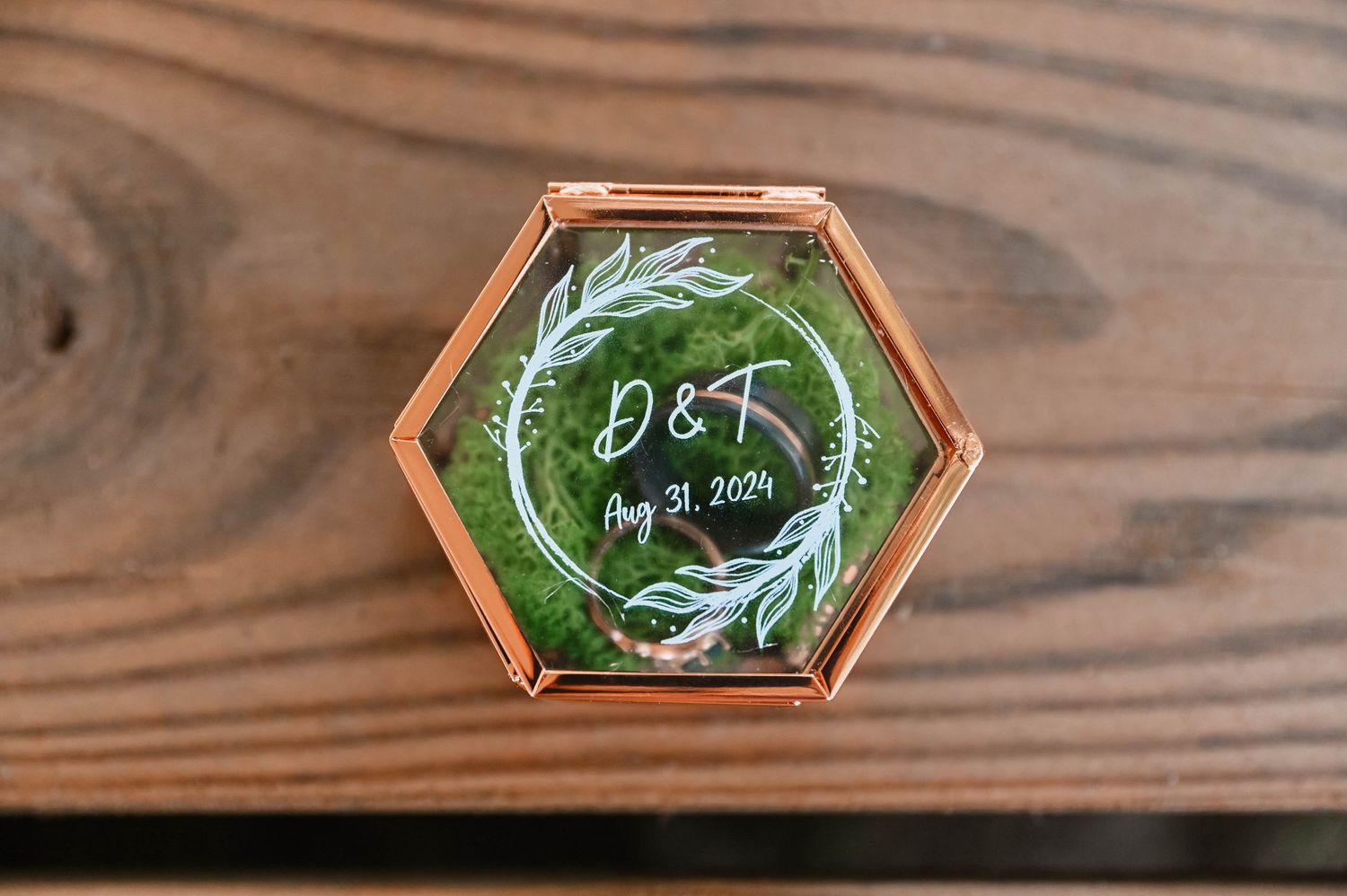 A hexagonal glass ring box with initials and greenery design.