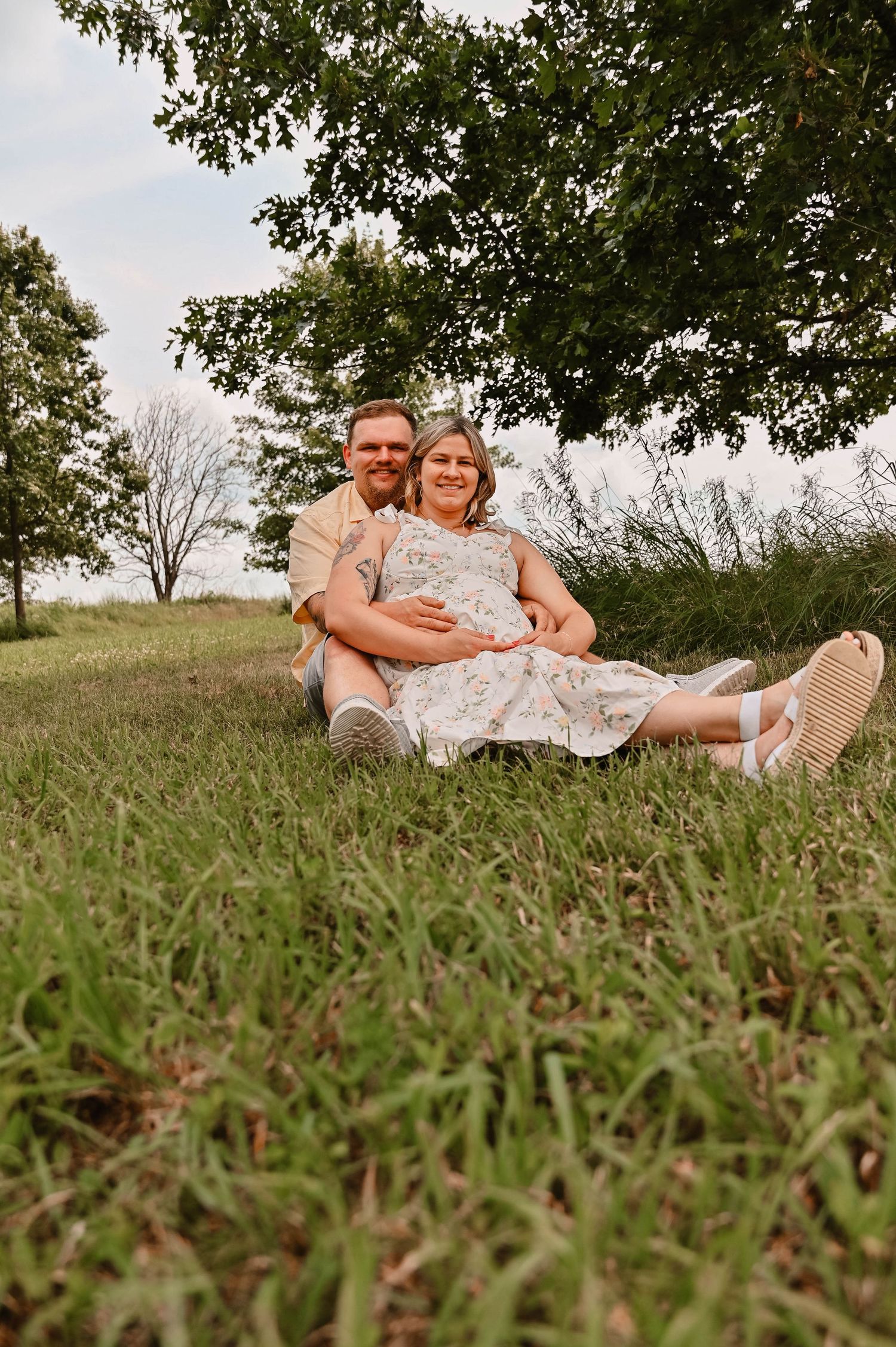 A couple relaxes together on grassy hillside during maternity photoshoot.