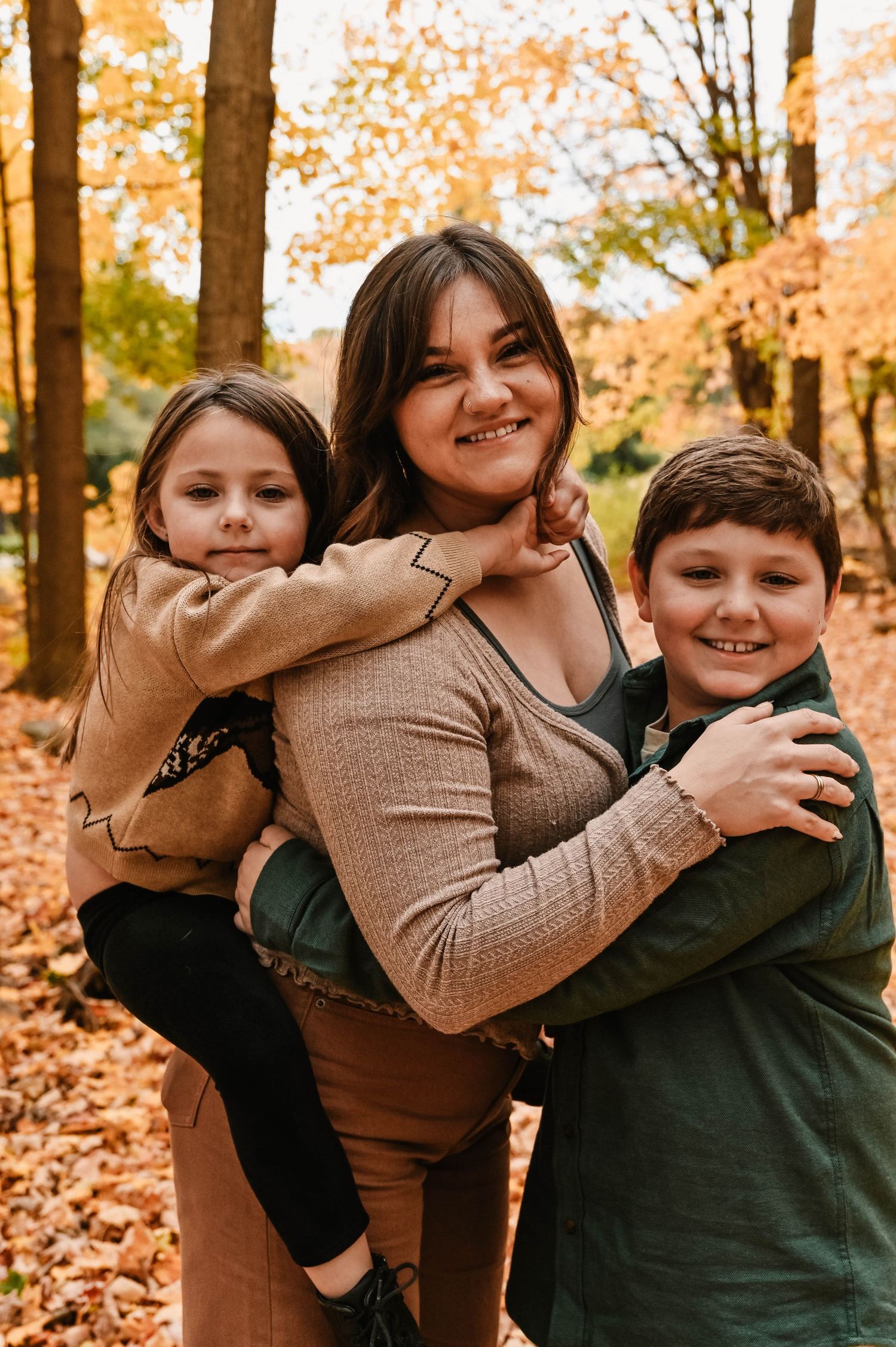 Playful family moment captured in a wooded area with golden fall foliage.