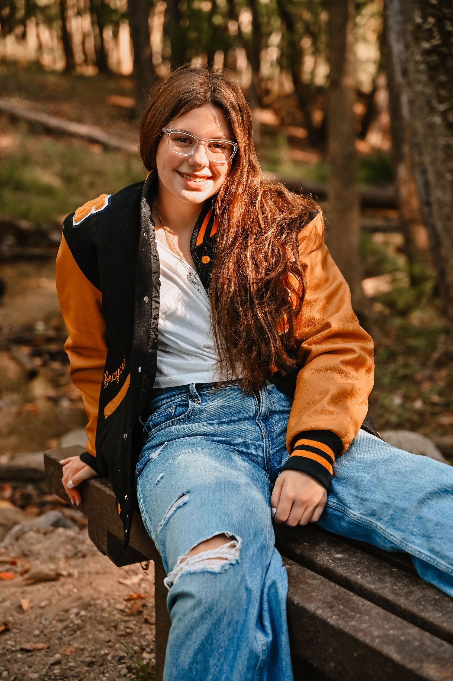Stylish varsity jacket and ripped jeans outfit photographed on wooden benches outdoors.