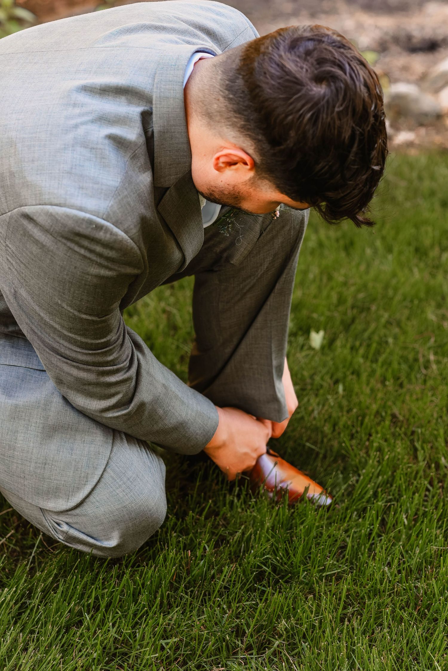 Person in grey suit crouching on grass searching for something.