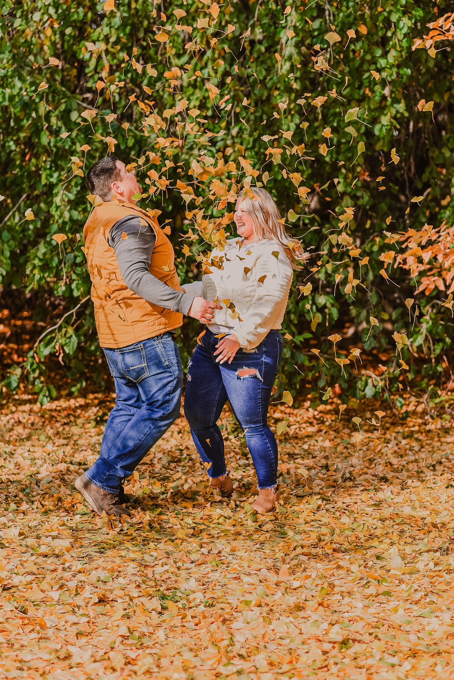 Playful couple dancing and spinning in fallen autumn leaves.