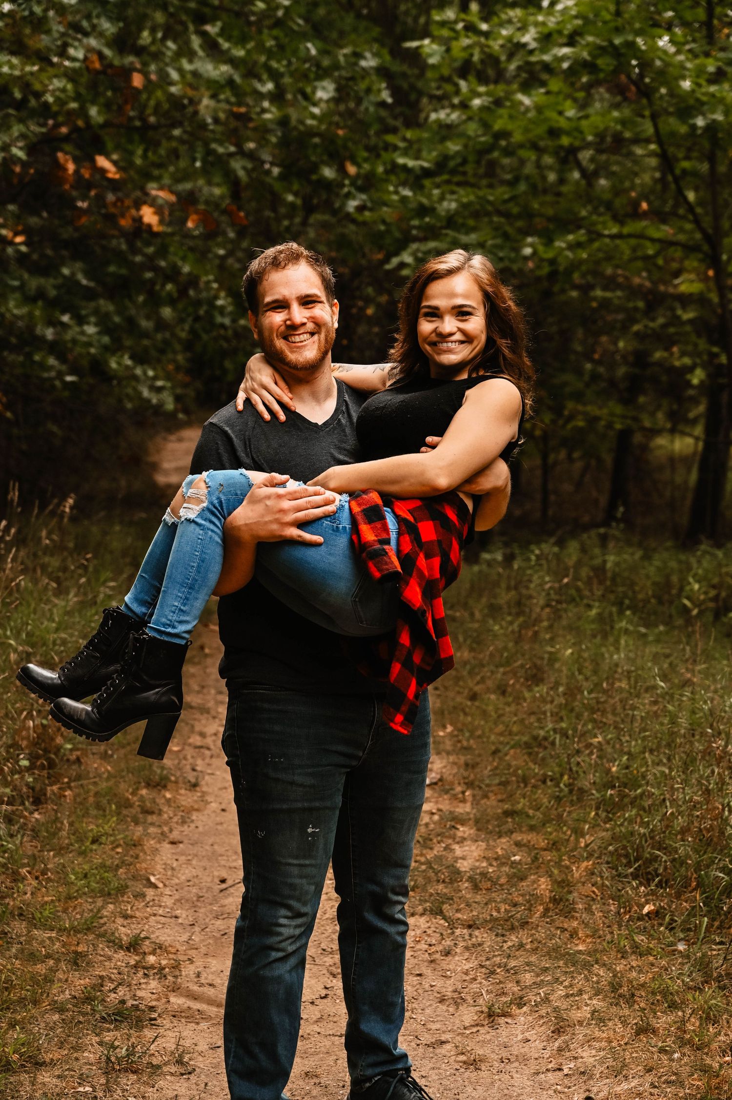 A couple shares a romantic moment on a dirt trail surrounded by autumn foliage.
