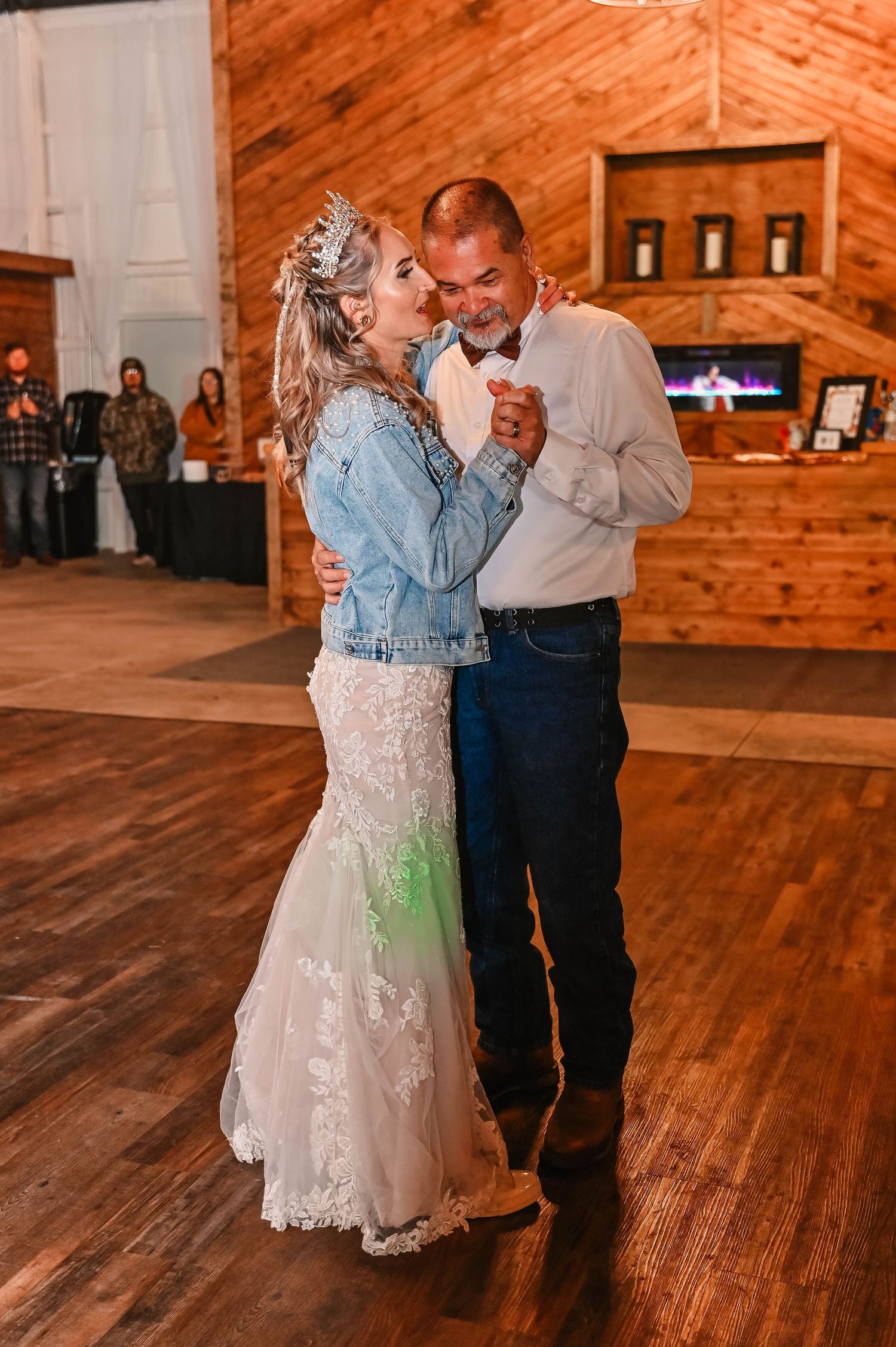 A couple sharing their first dance in a rustic wooden venue with the bride wearing a denim jacket over her gown.