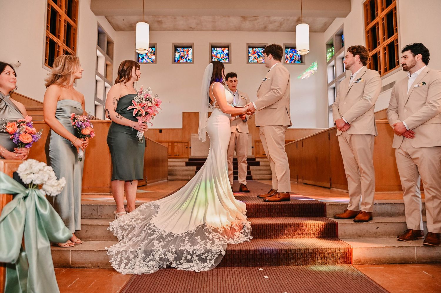 Wedding party lined up in formal attire inside a church with orange-tinted lighting.