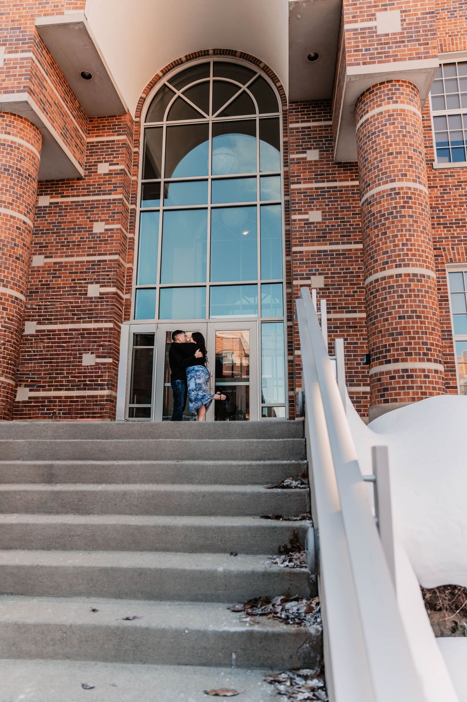 Red brick building entrance with arched windows and concrete steps.