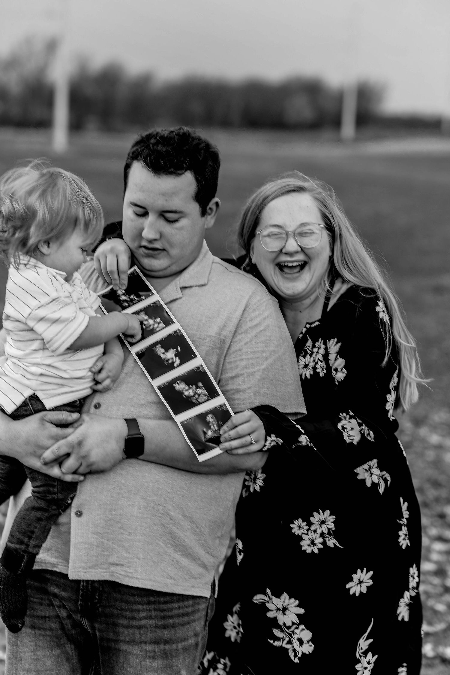 Family shares emotional moment while holding ultrasound photos in black and white.
