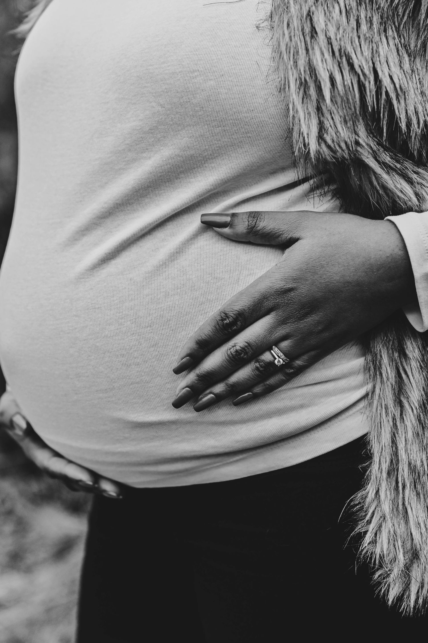 Close-up black and white photo of hands resting on a white maternity shirt.
