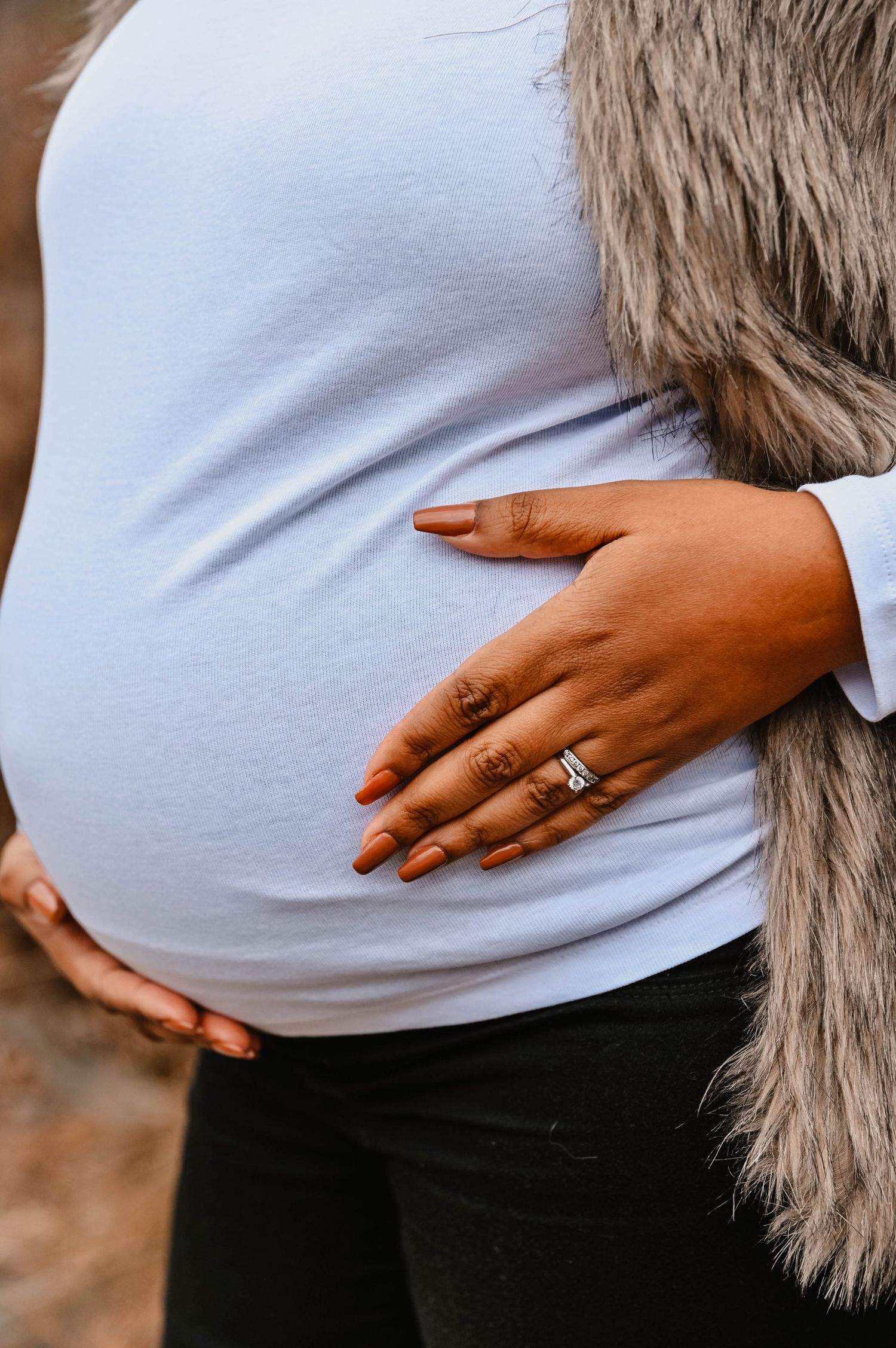 Close-up of hands resting on a white sweater, showing an engagement ring.