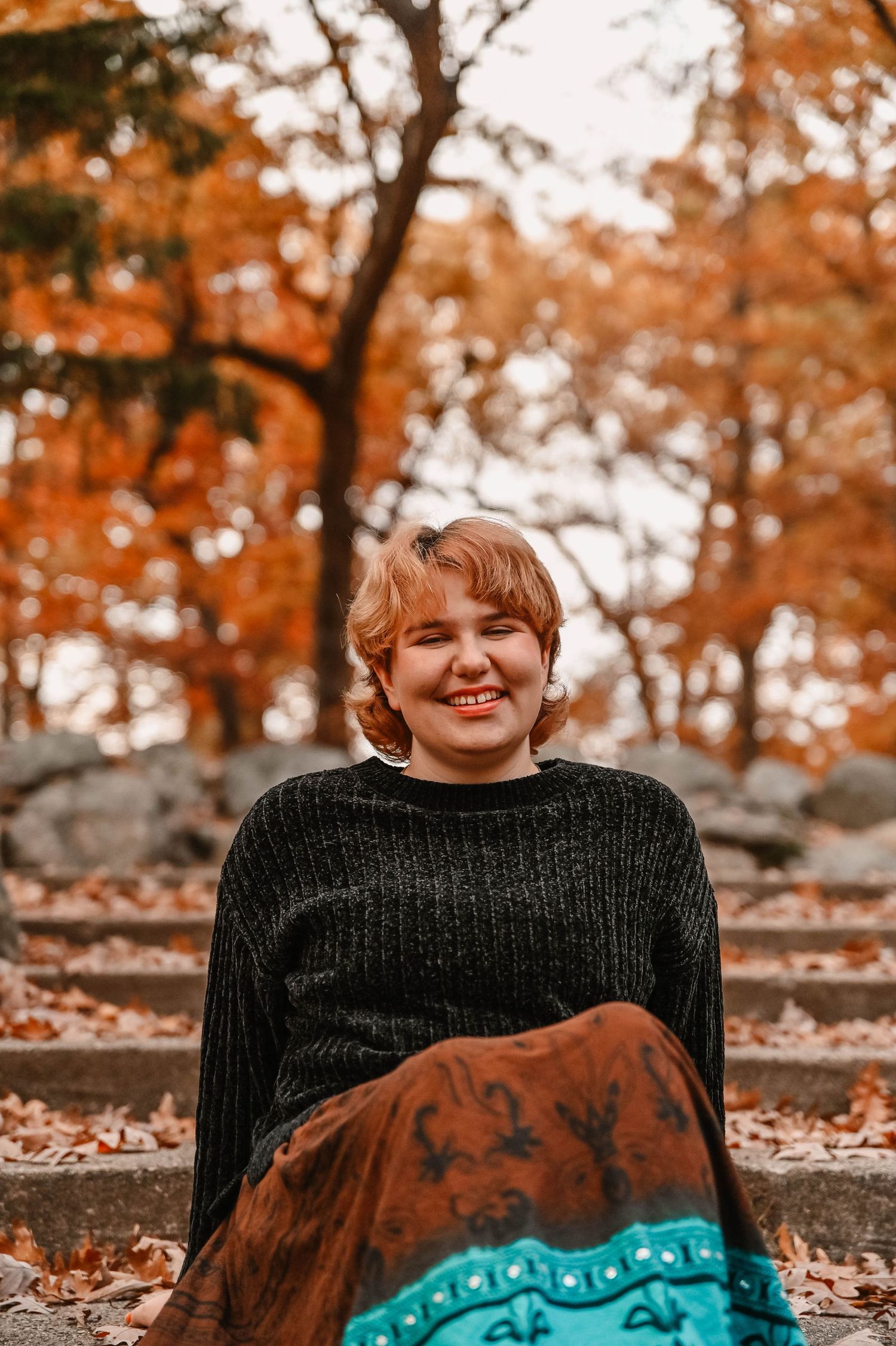 Black sweater and patterned blanket styled against autumn leaves and stone wall.