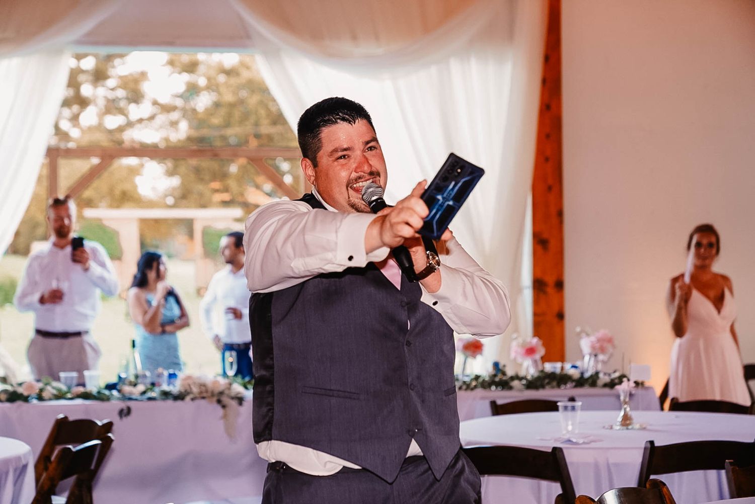 A person in a vest holds up a camera while taking photos at a wedding reception.