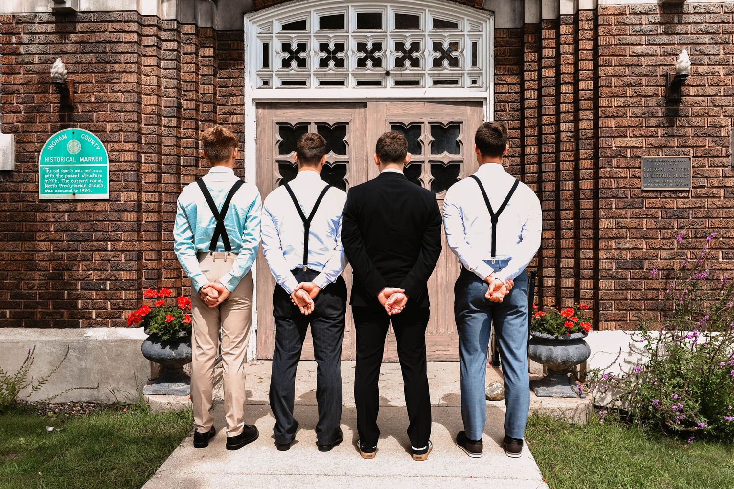Groomsmen pose for photos in front of a brick church entrance.