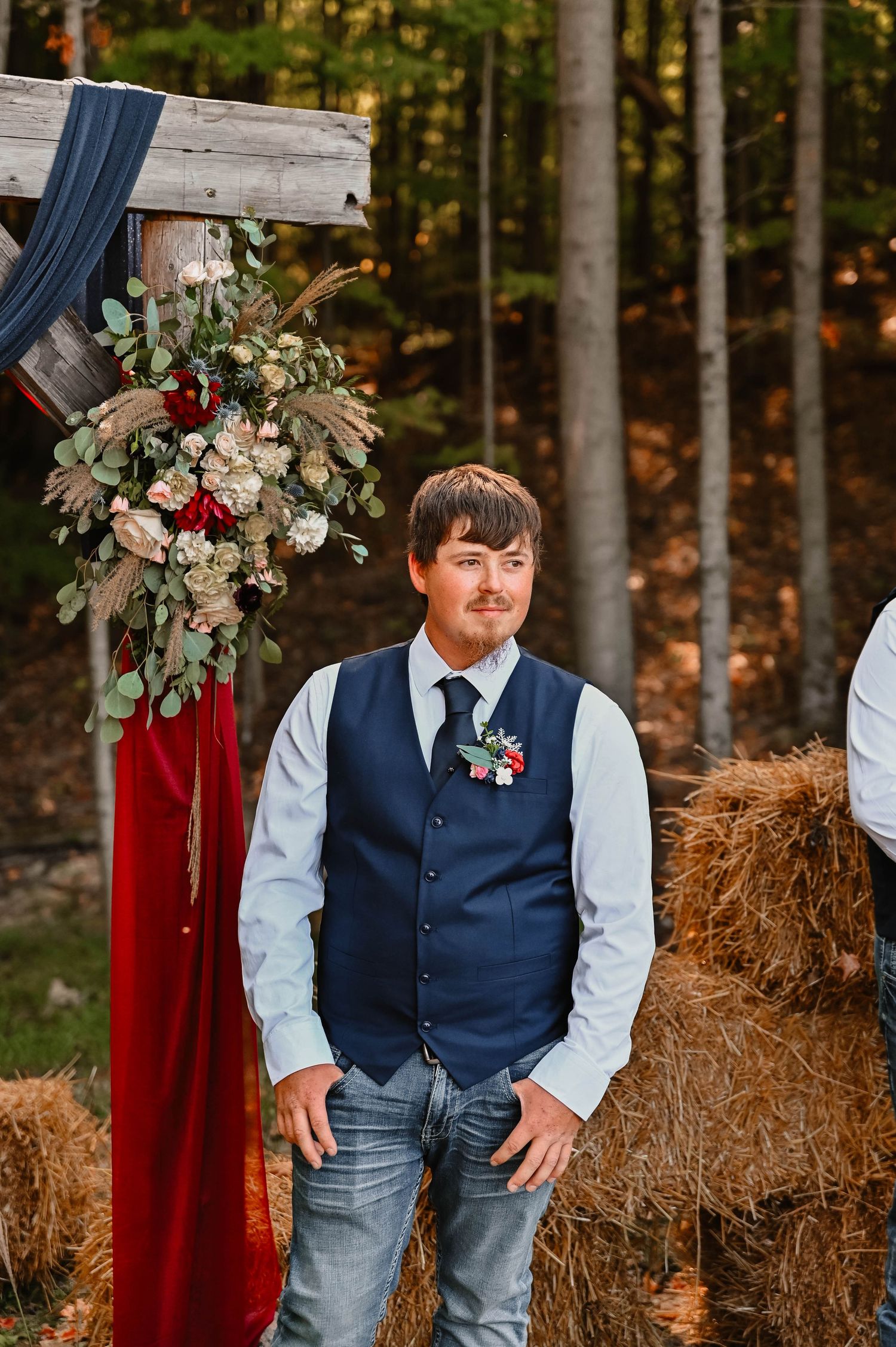 A child in formal attire smiles while standing in front of rustic wedding decor.