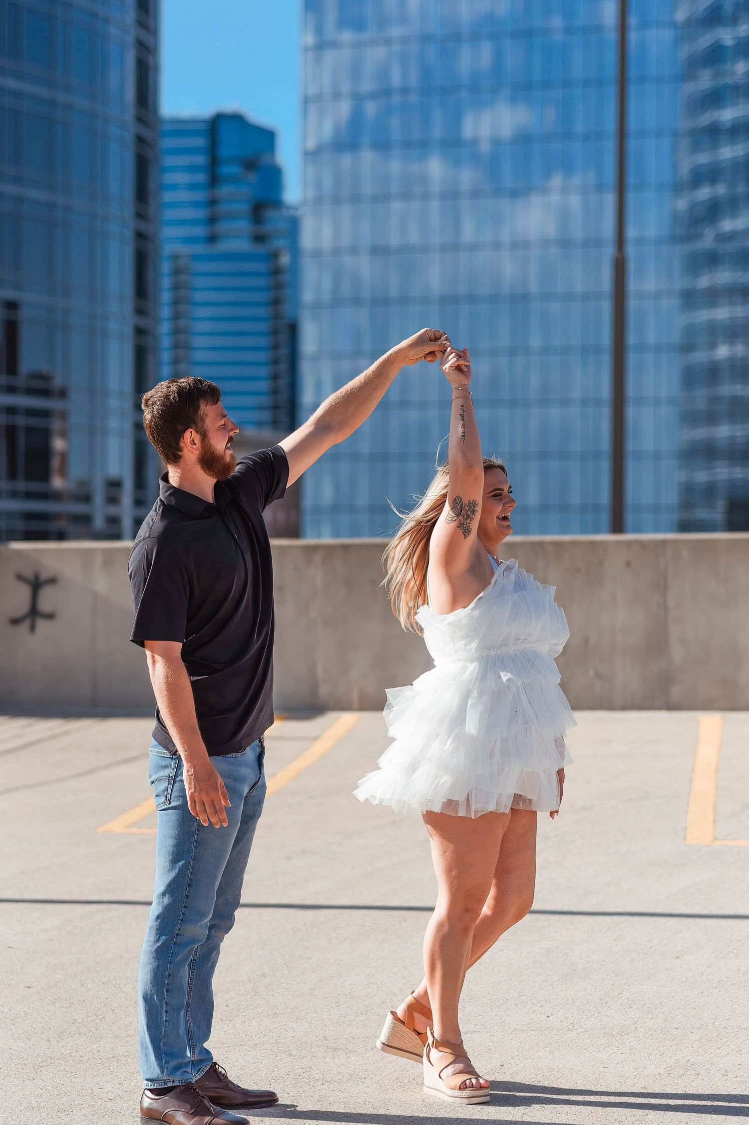 A couple dances playfully on an urban rooftop with city buildings in the background.