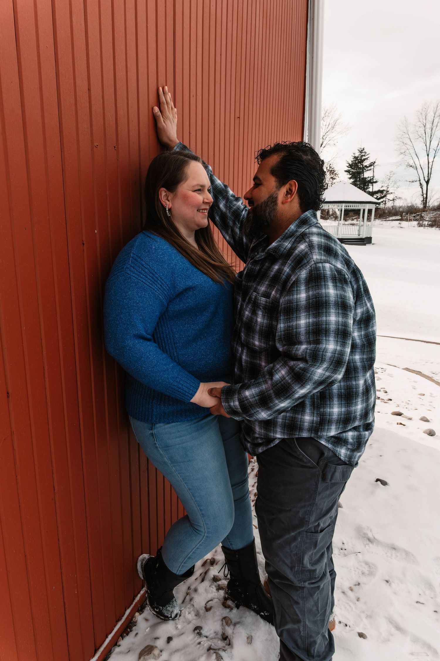 Romantic couple moment against red wooden wall in snowy setting.