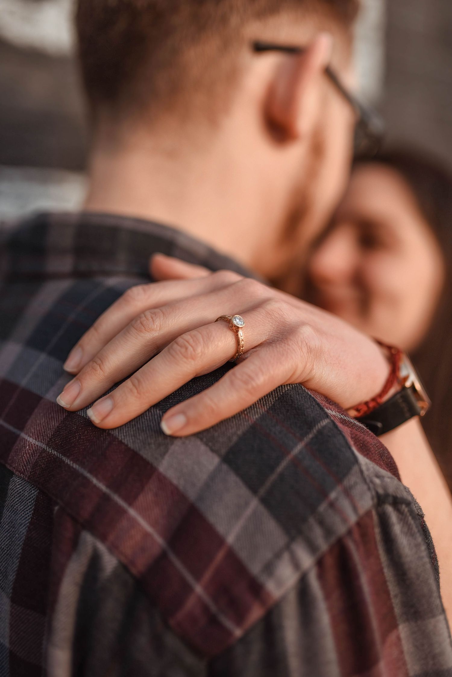 Close-up shot of hands embracing showing an engagement ring and plaid shirt details.