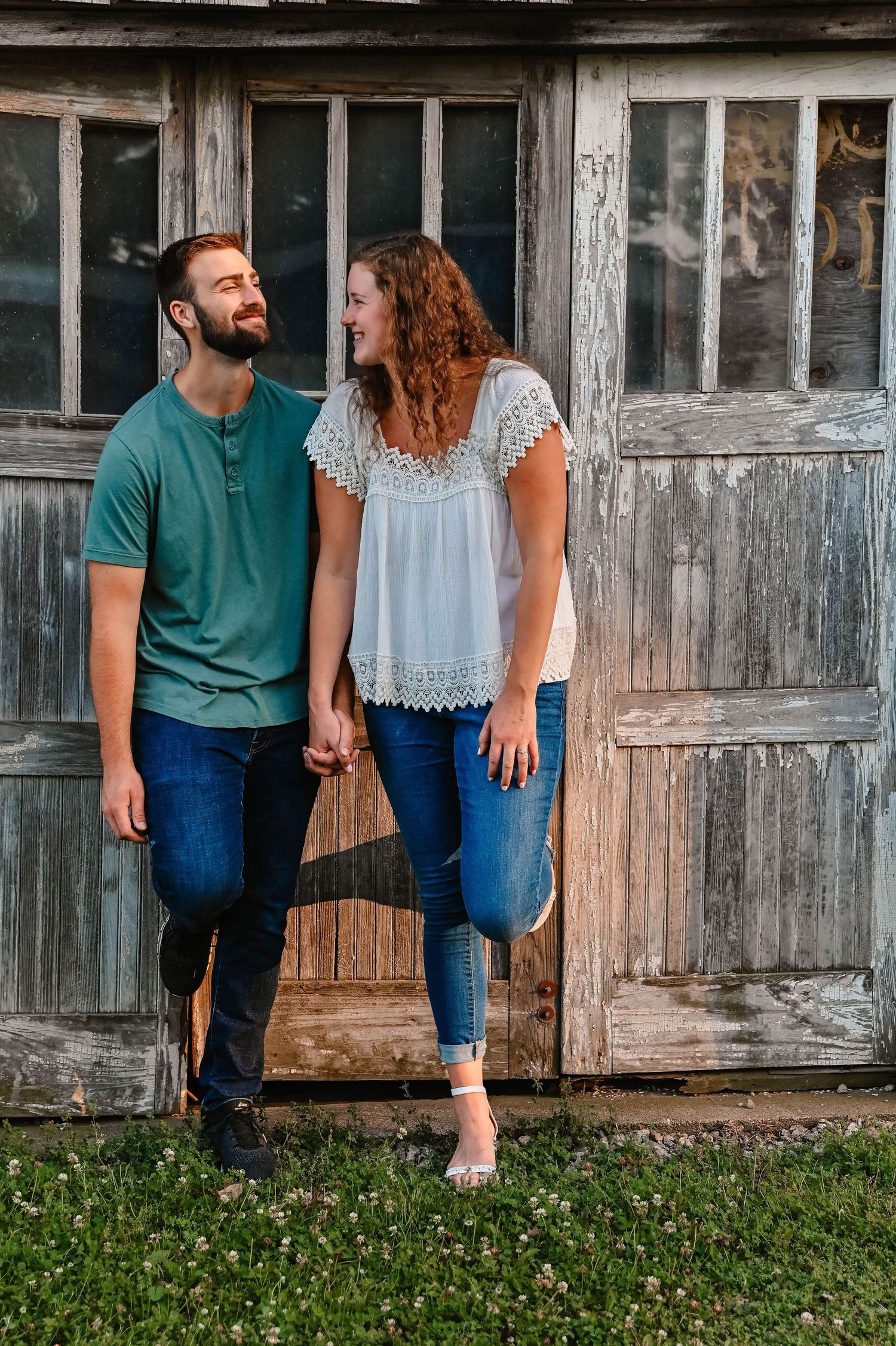 Couple walking and laughing together by rustic wooden barn wall.