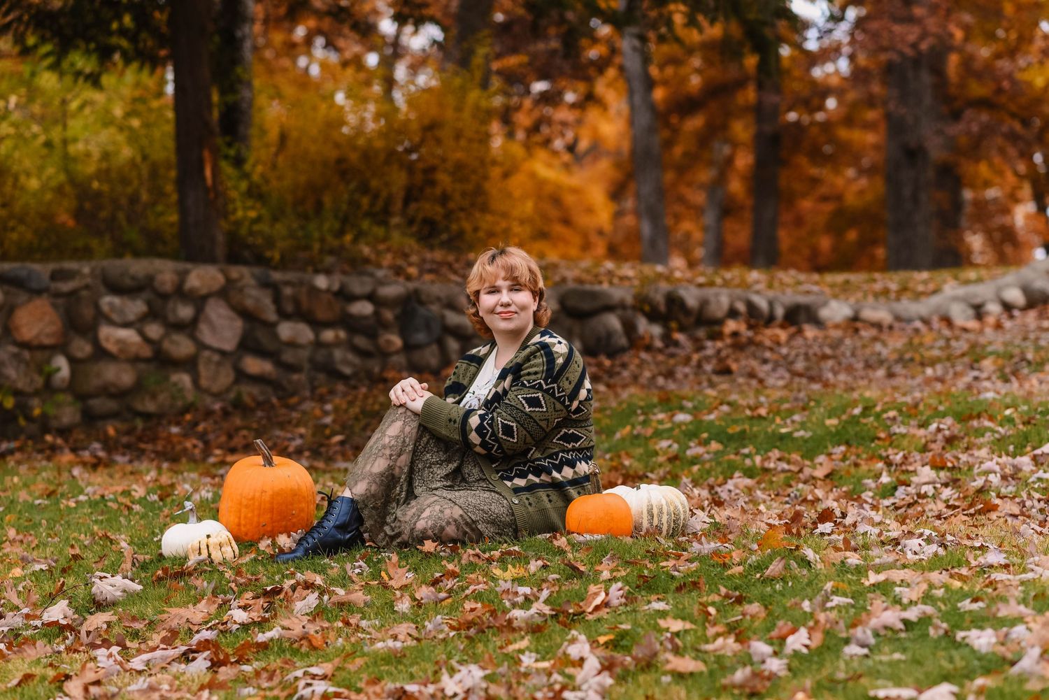 Fall themed portrait with pumpkins and stone wall amid autumn foliage.