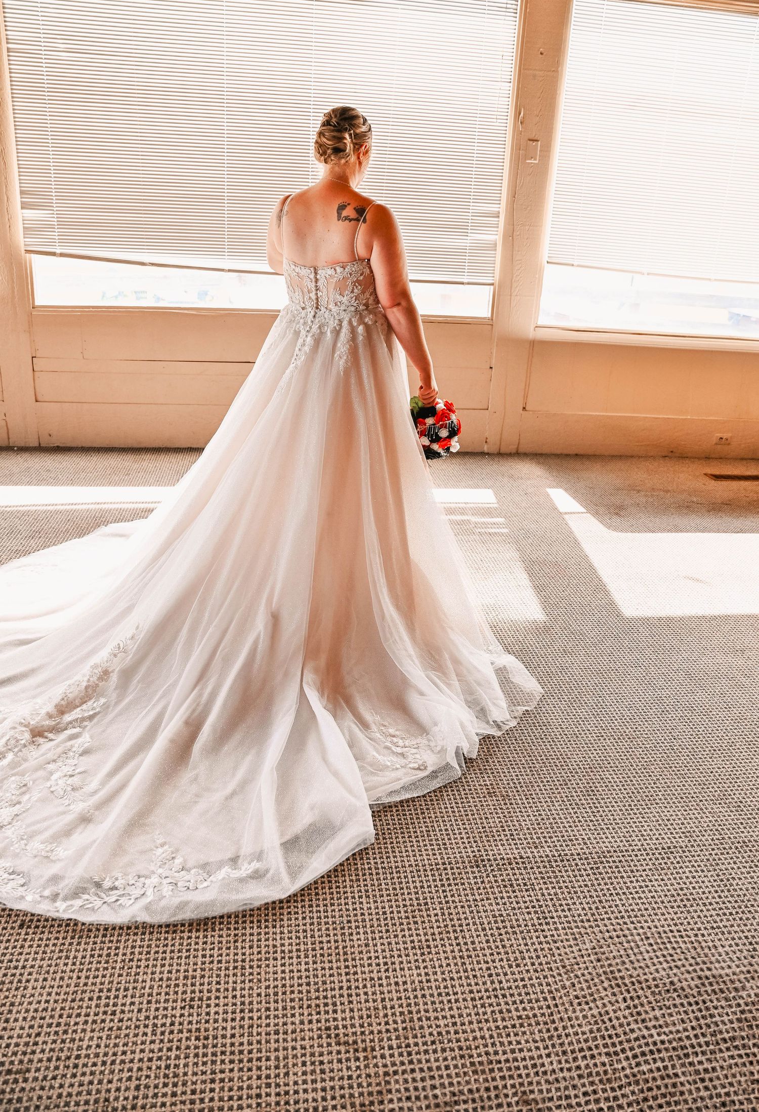A flowing white wedding dress with lace details and long train photographed from behind in natural light.