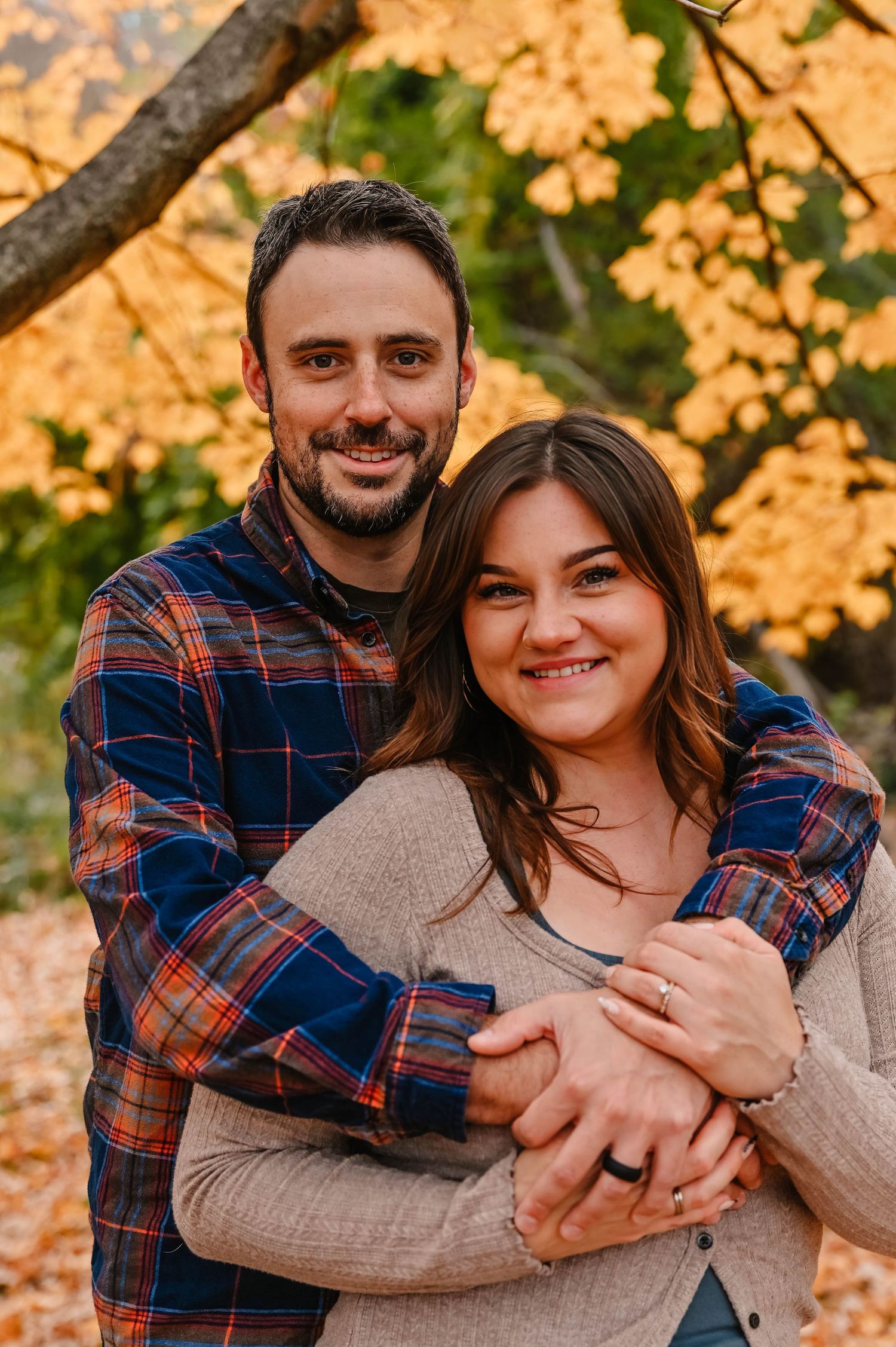 Couple embracing in warm autumn sunlight with golden leaves in background.